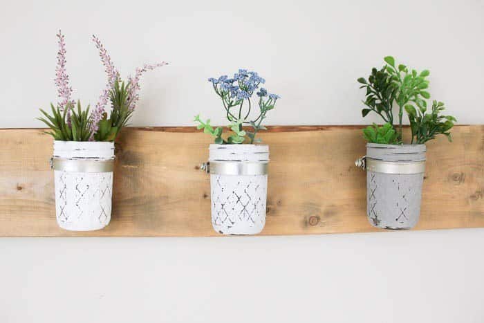 3 distressed mason jars with potted plants in them hung on a rustic farmhouse piece of wood 