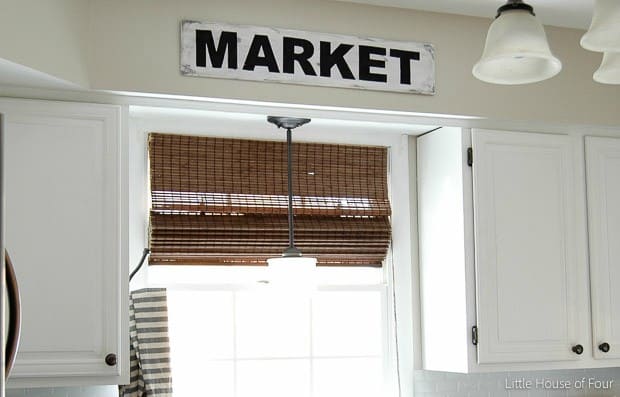 Custom farmhouse sign that says "market" hung over a sink and window in a kitchen with rustic touches and bright light