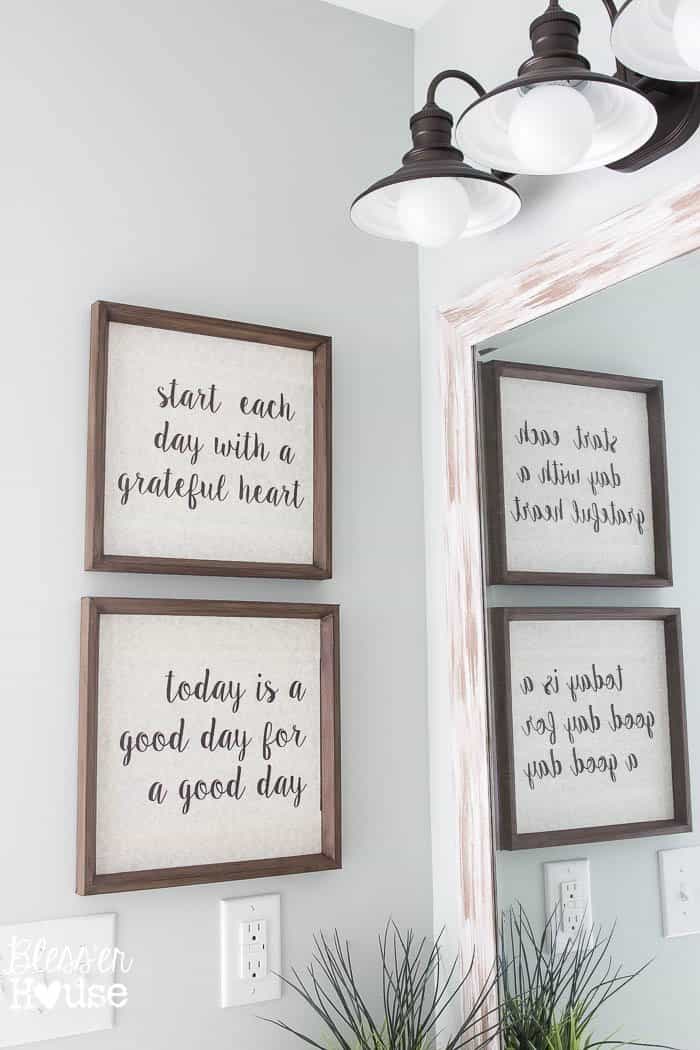 two framed quotes talking about the day hung up on a wall in a bathroom with a mirror reflection