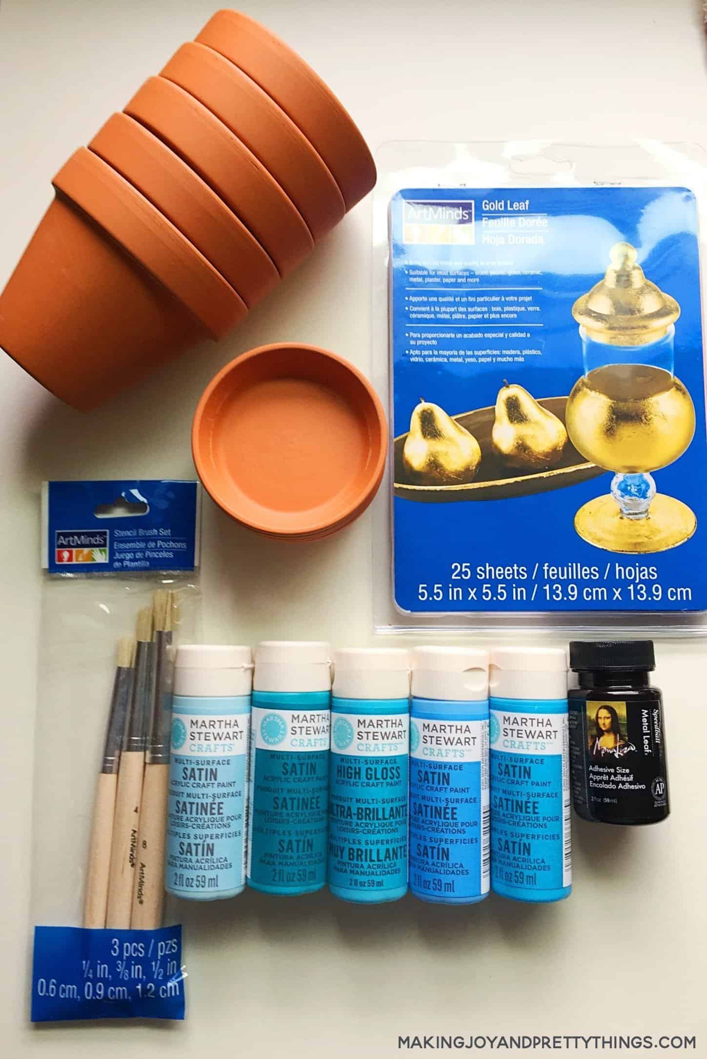 Supplies for gold leaf planters painted in blue and transformed clay pots with gold notes applied with a spray adhesive