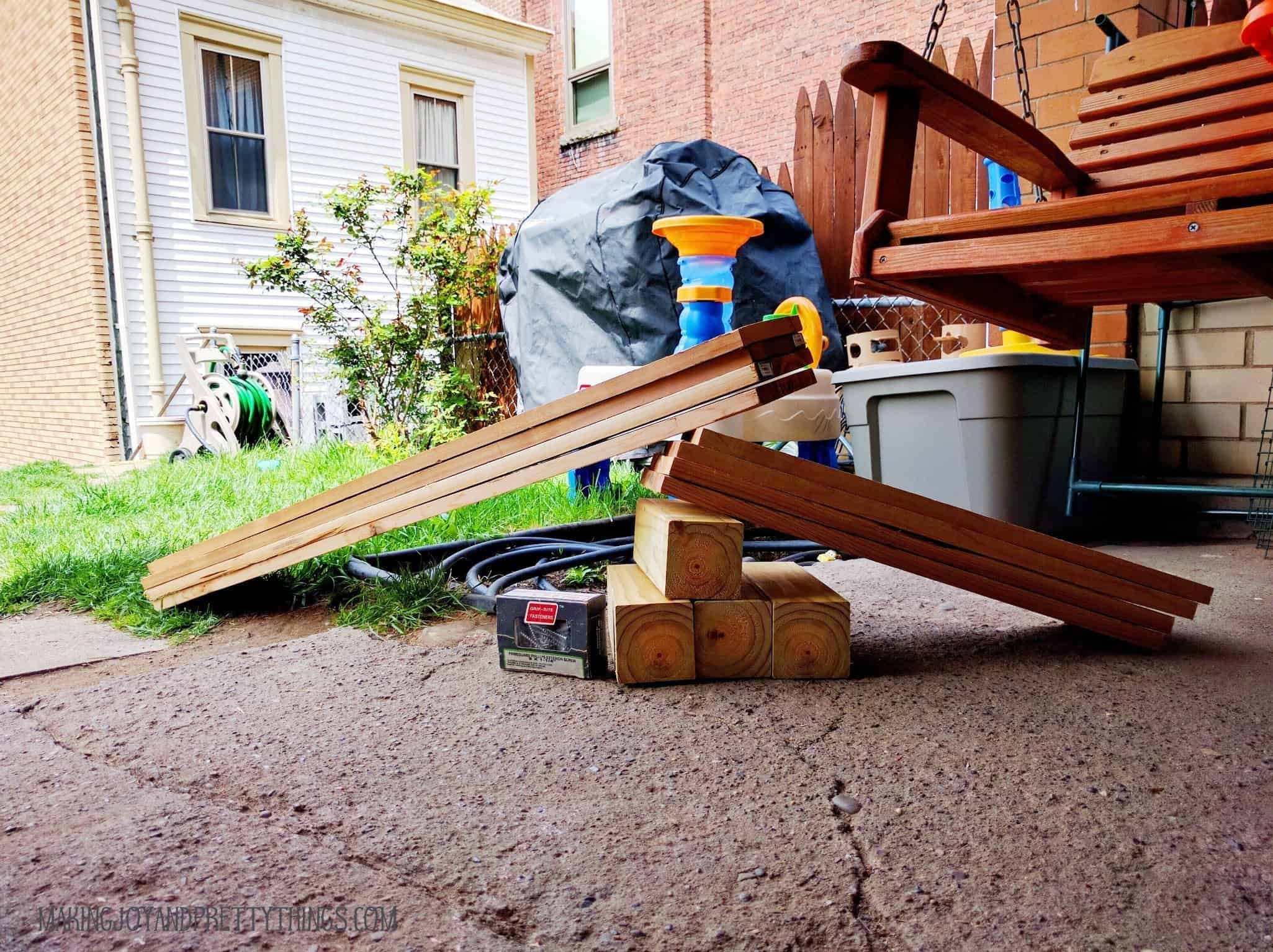 Supplies for a tutorial on how to build a cedar raised garden bed including cedar board and screws