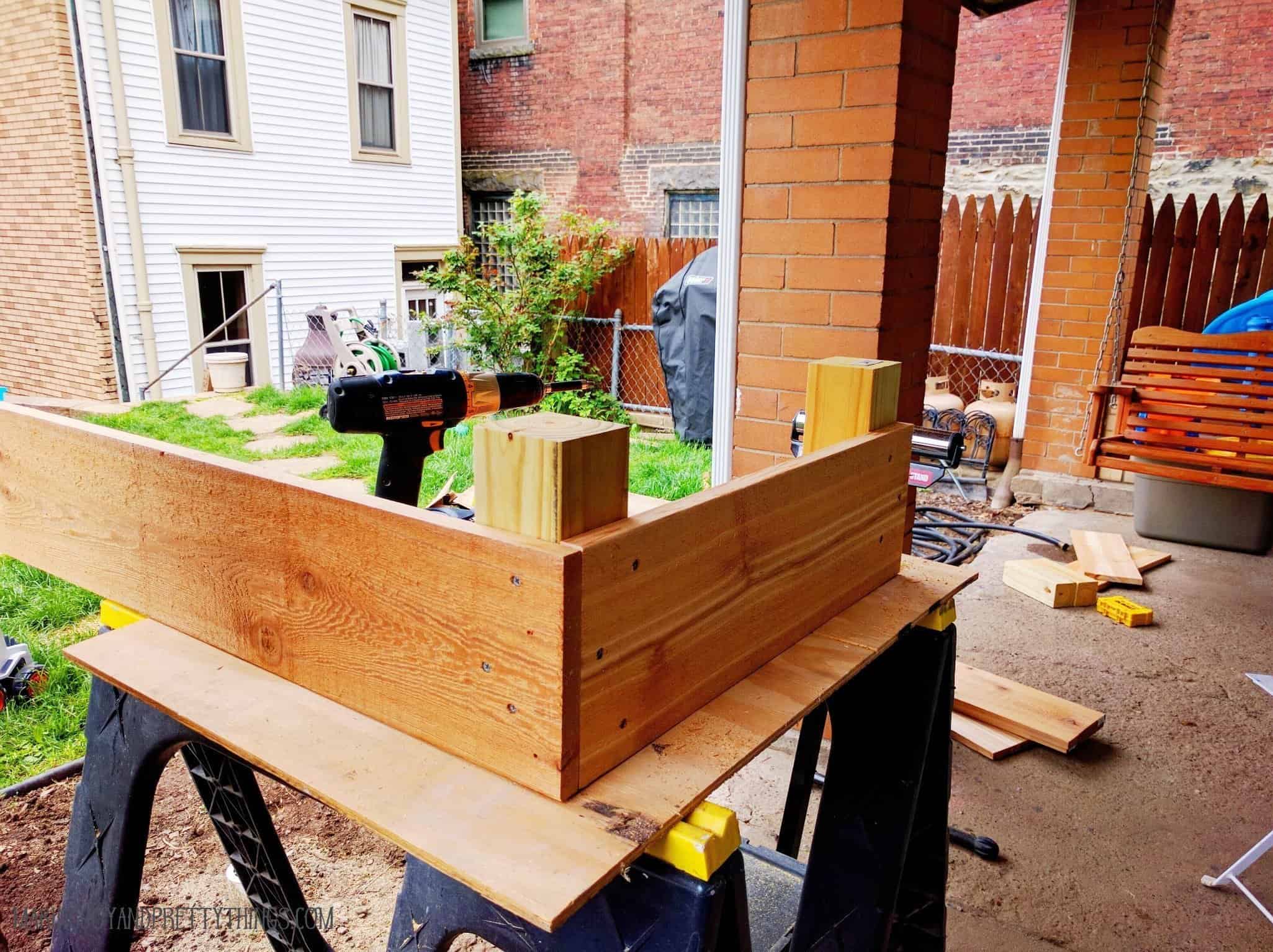 Screwing in cedar board into posts overlapping sides to build up the cedar raised garden bed