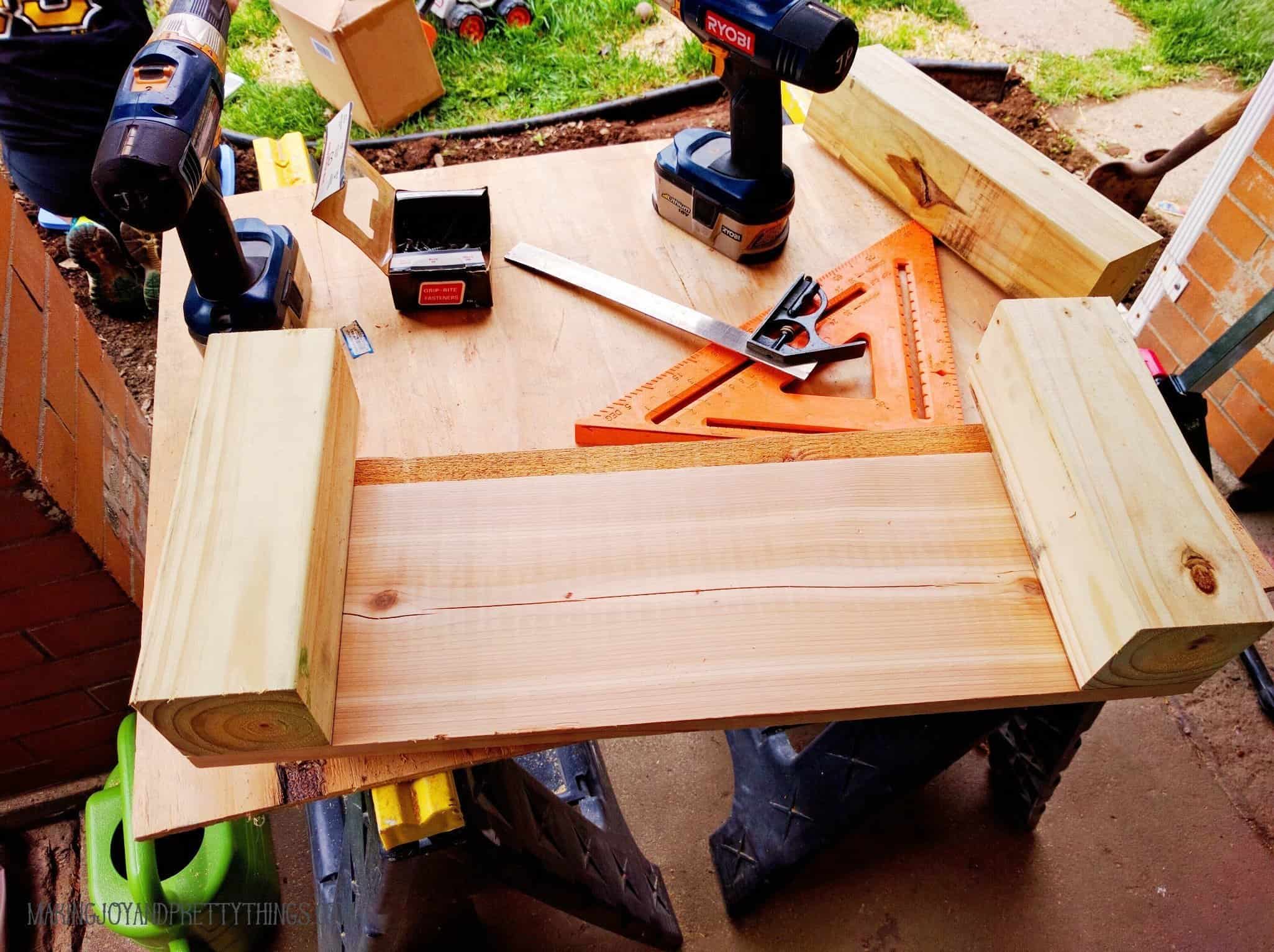 Assembled side of a cedar raised garden bed on a work table with drills and other tools to help put the bed together