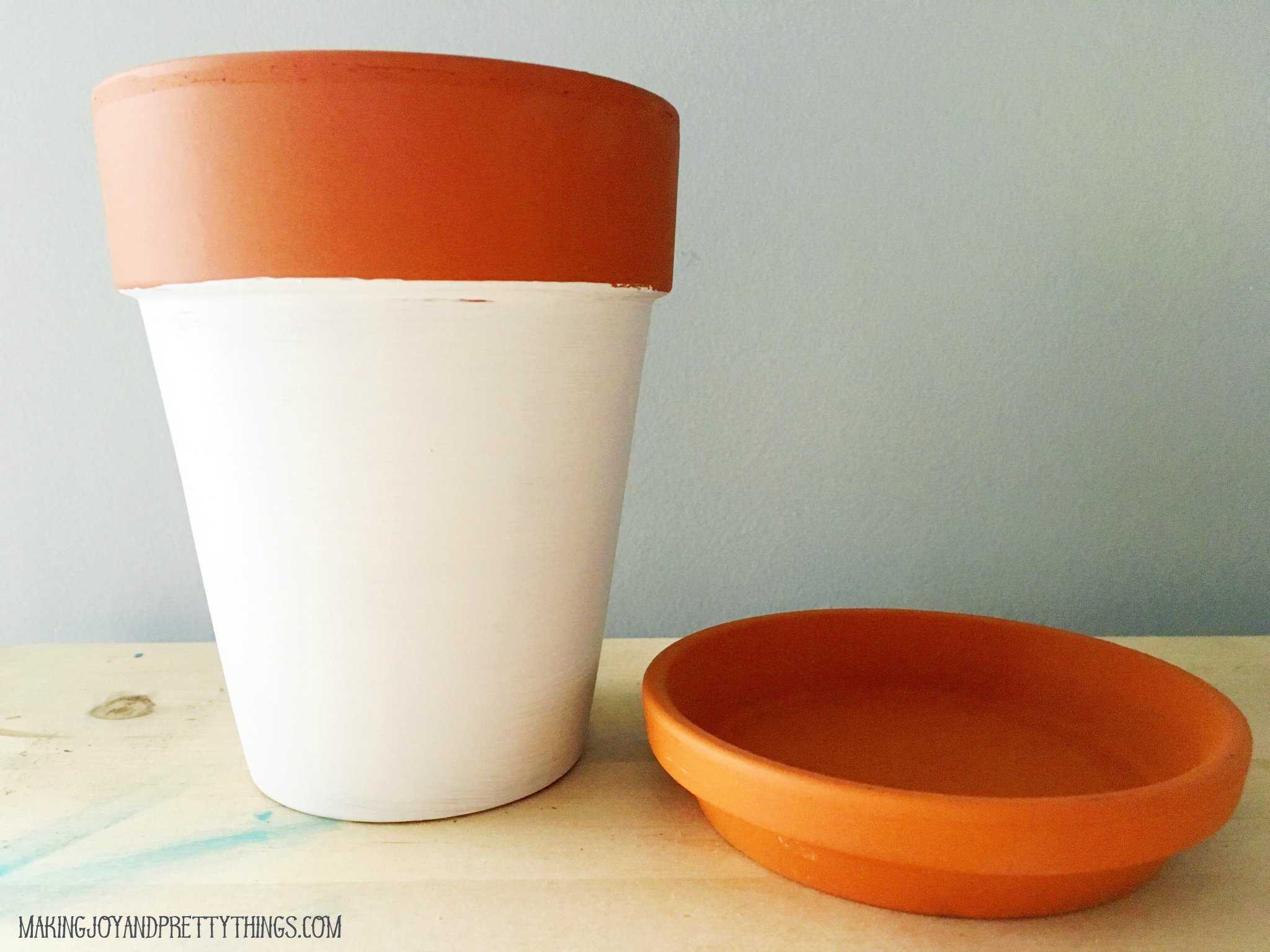 A terra cotta planter with a separate saucer. The bottom half of the pot is painted white, while the top rim and saucer remain a natural terra cotta color.