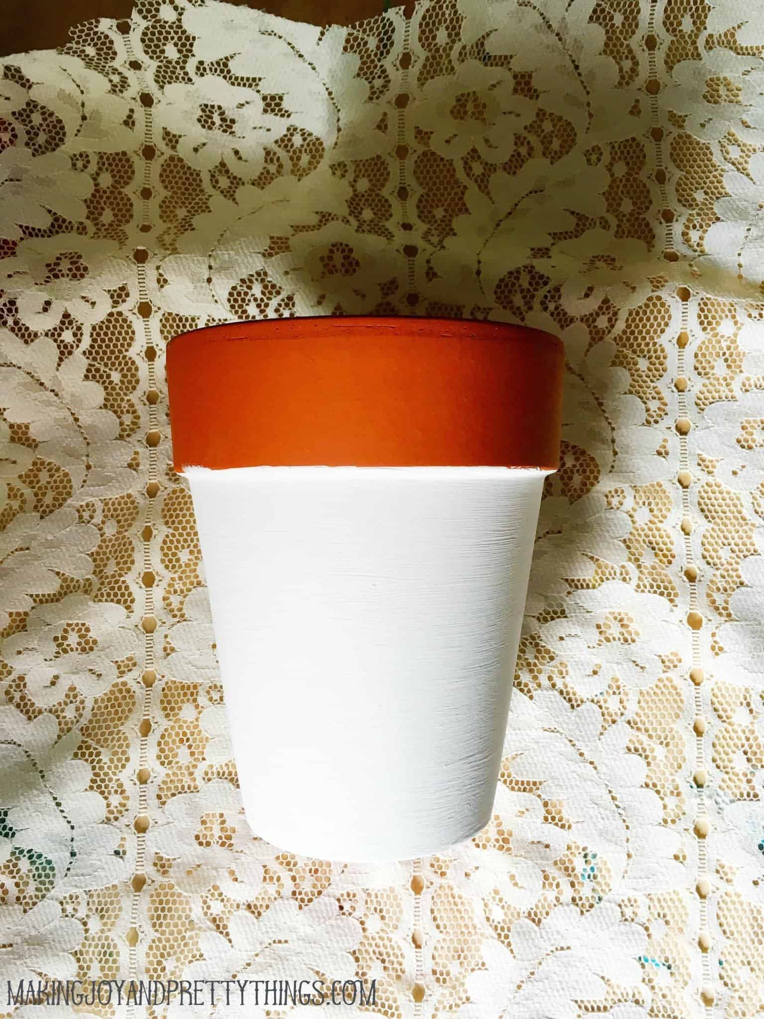 A partially painted terra cotta pot sits on a sheet of white lace fabric.