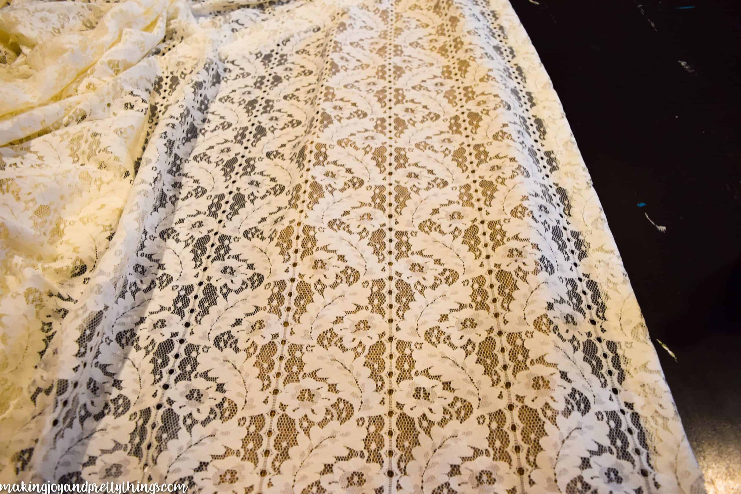 Intricate white lace curtains with a floral pattern are laid out on a black table.