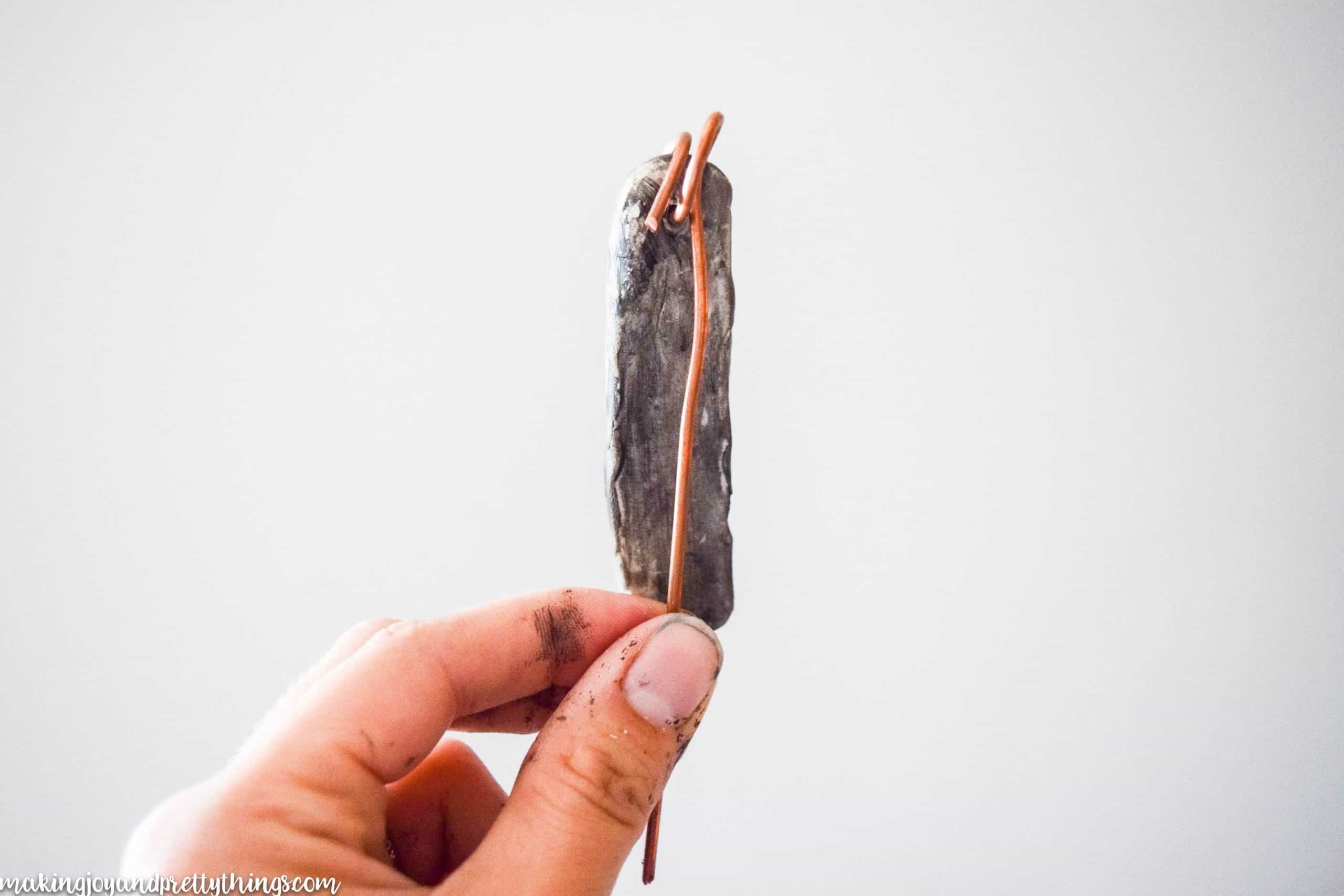 Holding a potted plant label made with copper wire and oven baked clay hardened to put into a garden