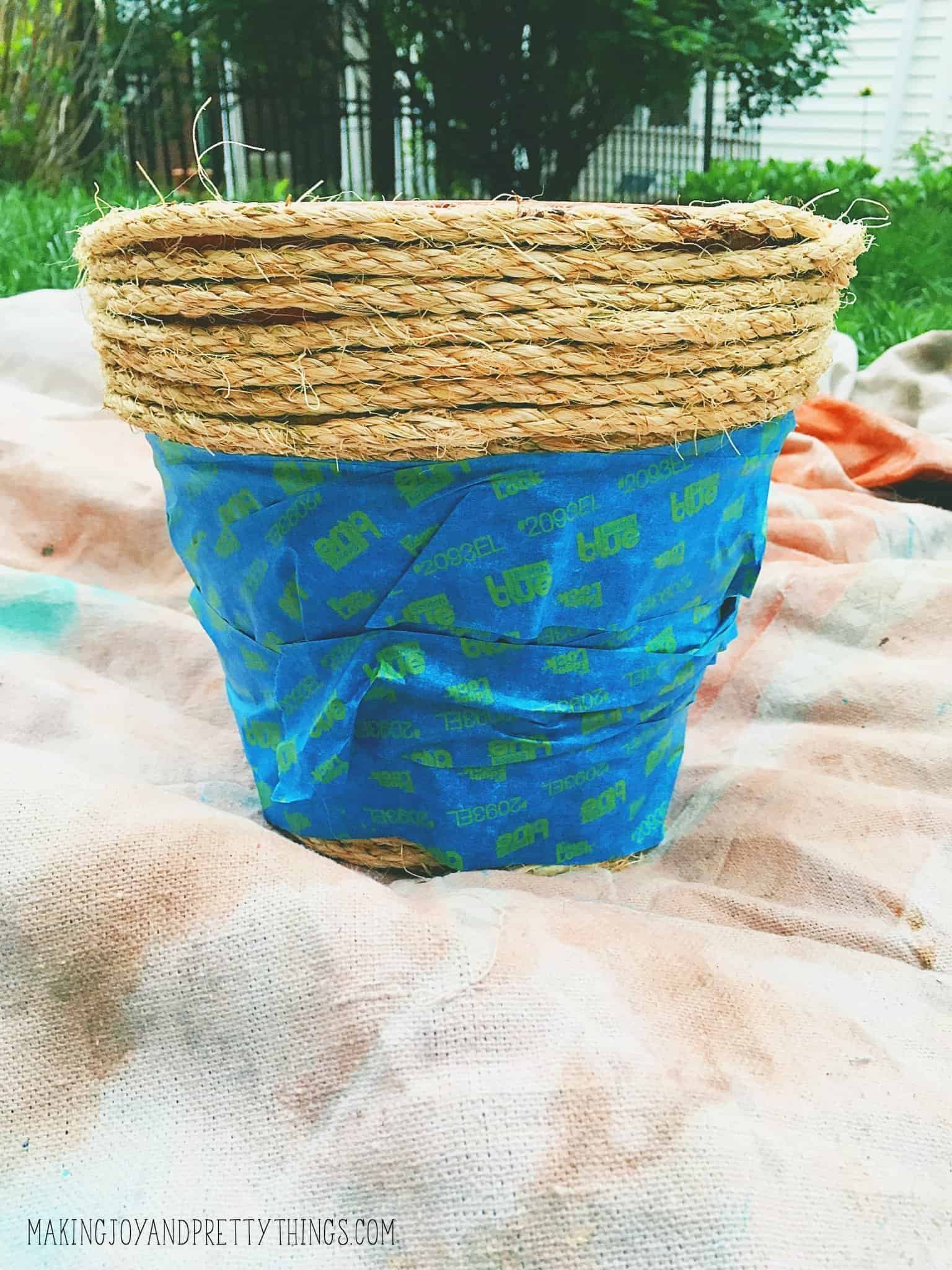 Taping off the bottom of a pot that has been wrapped to paint a color tone on the top that will be different from the bottom.