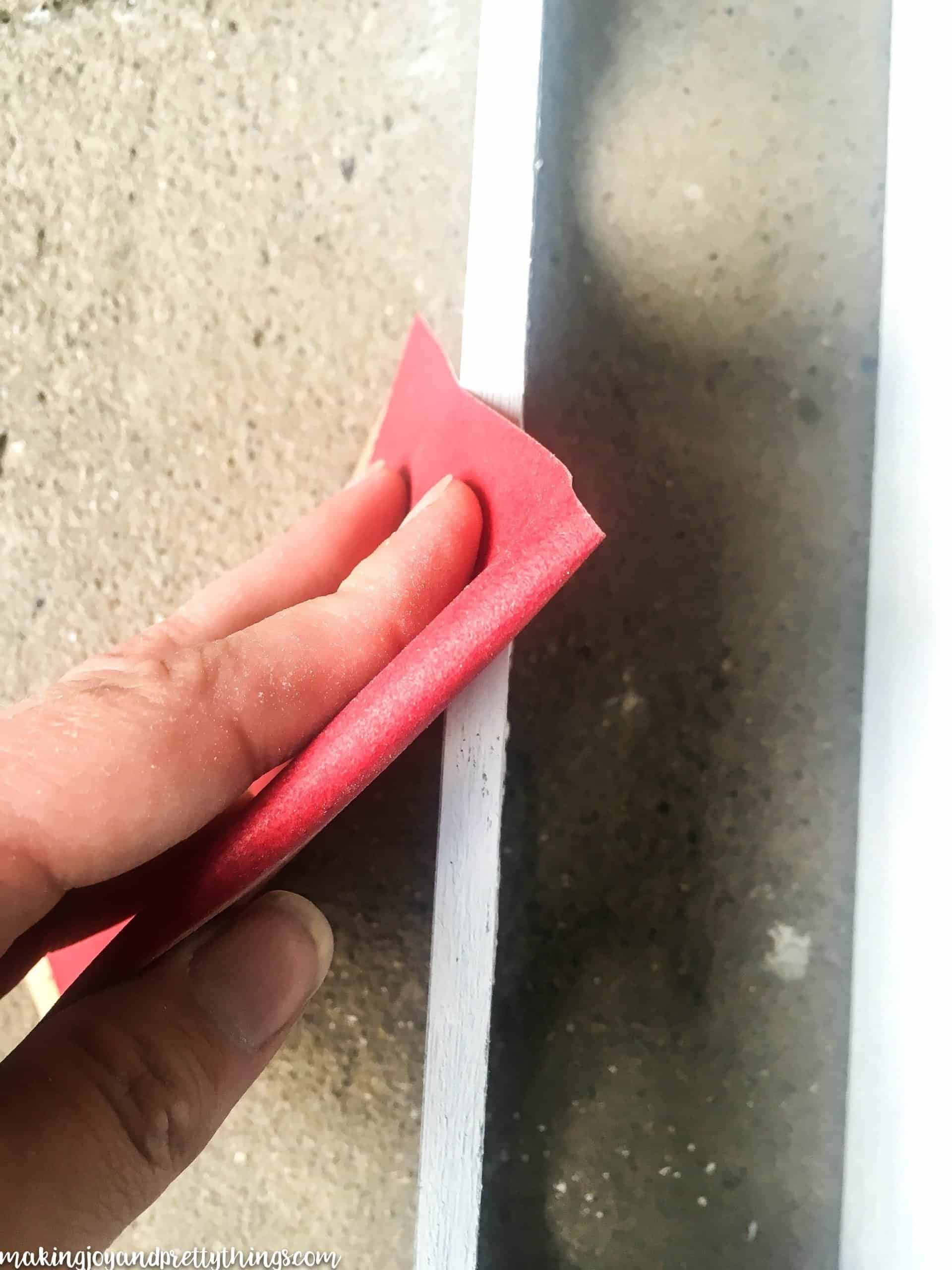 A hang holding a piece of red sandpaper, sanding down the painted surface of a wooden box to give it a distressed finish.