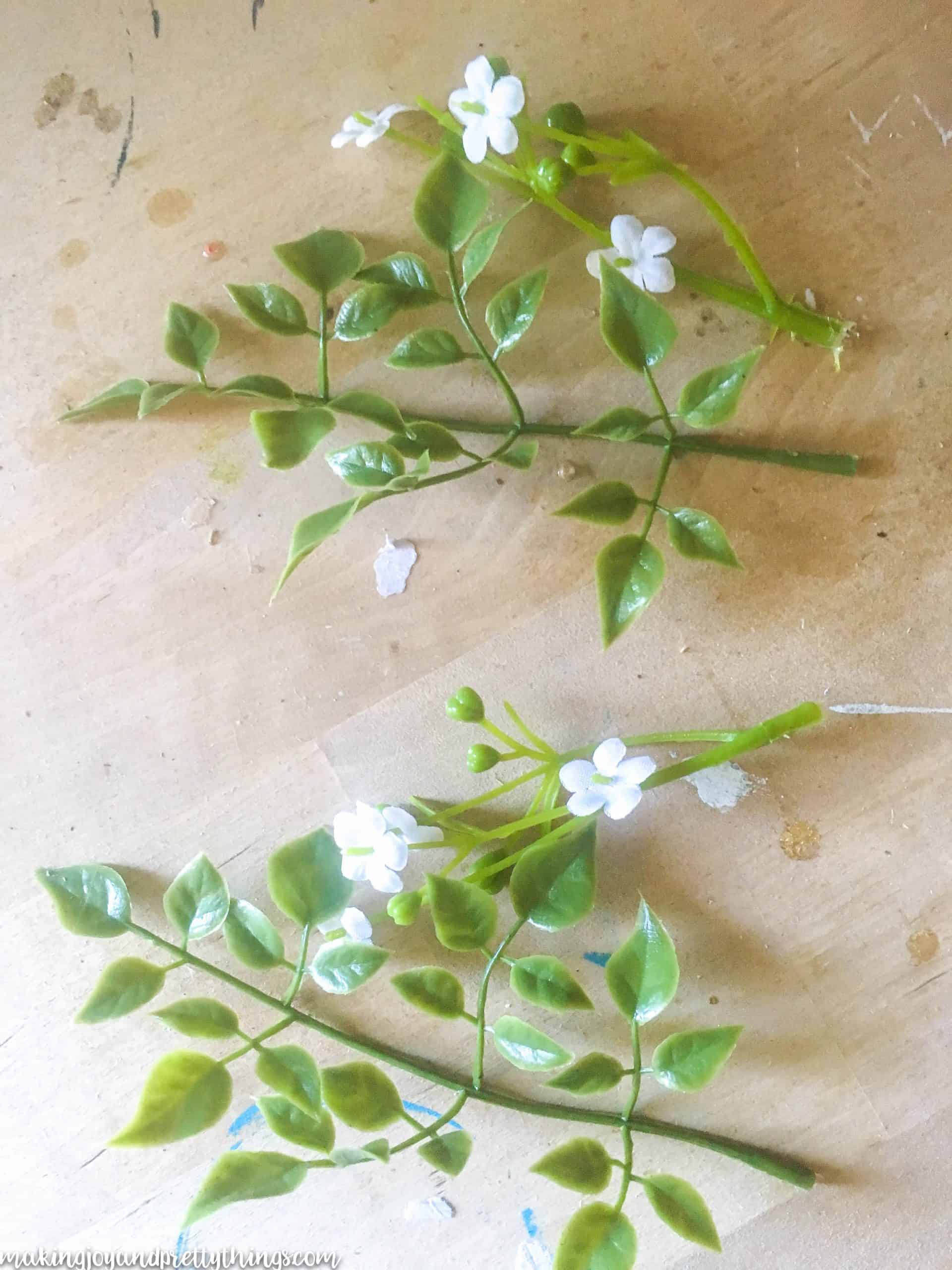 Small sprigs of faux greenery and baby's breath flowers sit on a wooden work table.