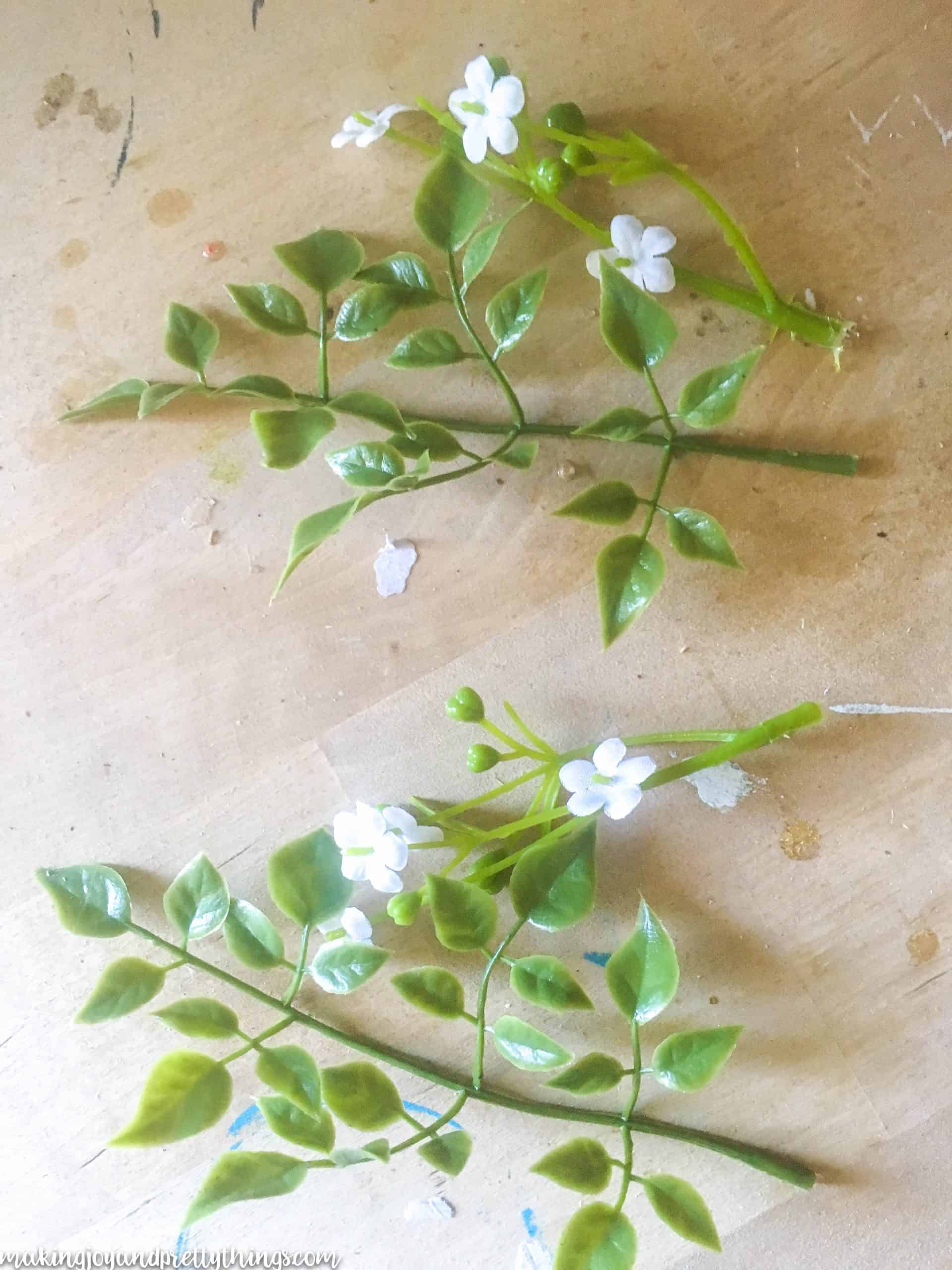 Springs of faux greenery with small white baby's breath flowers sit on a wood table.