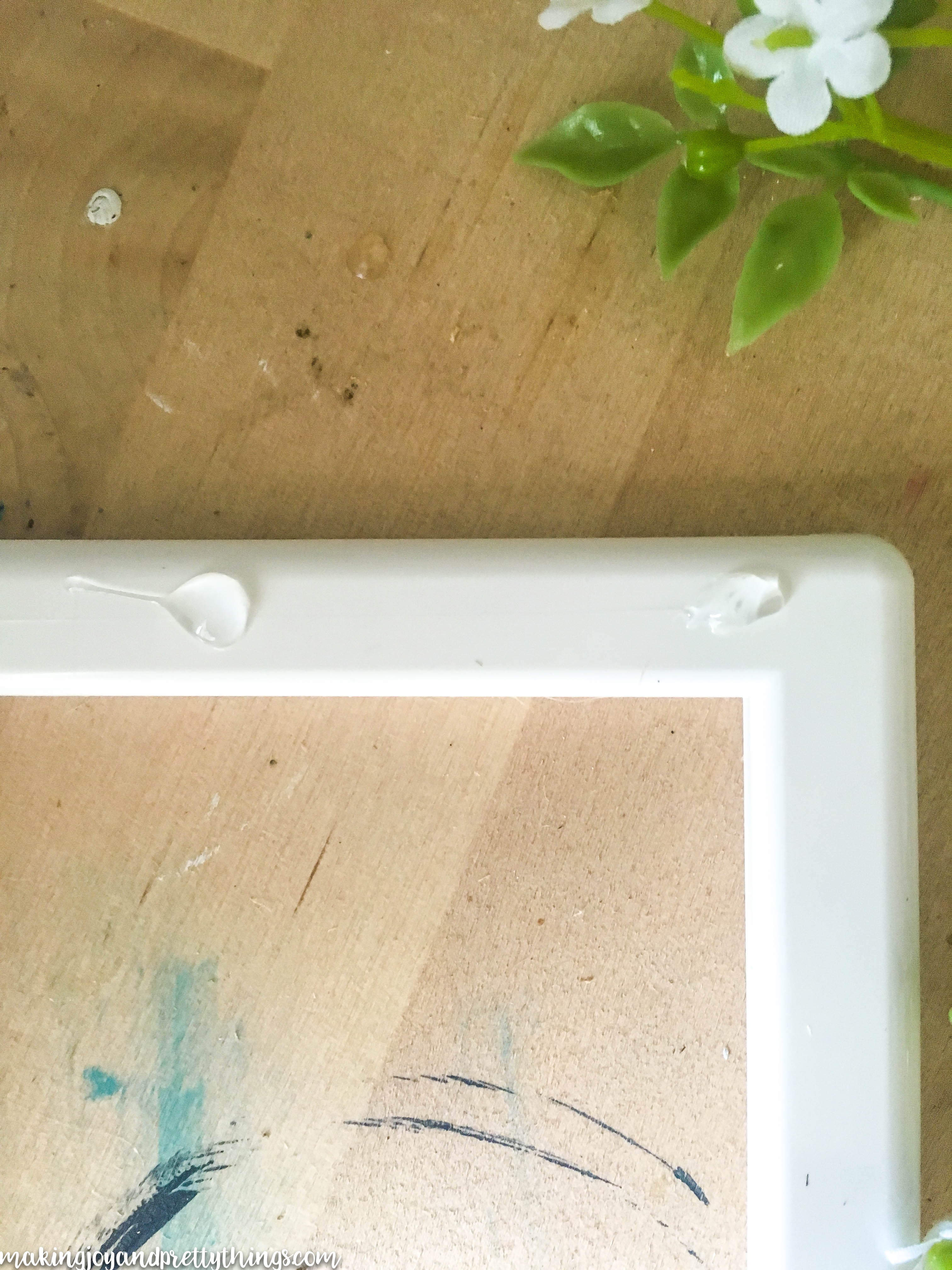 A close-up look at the corner of the white picture frame, with two dots of hot glue applied about an inch apart from each other.