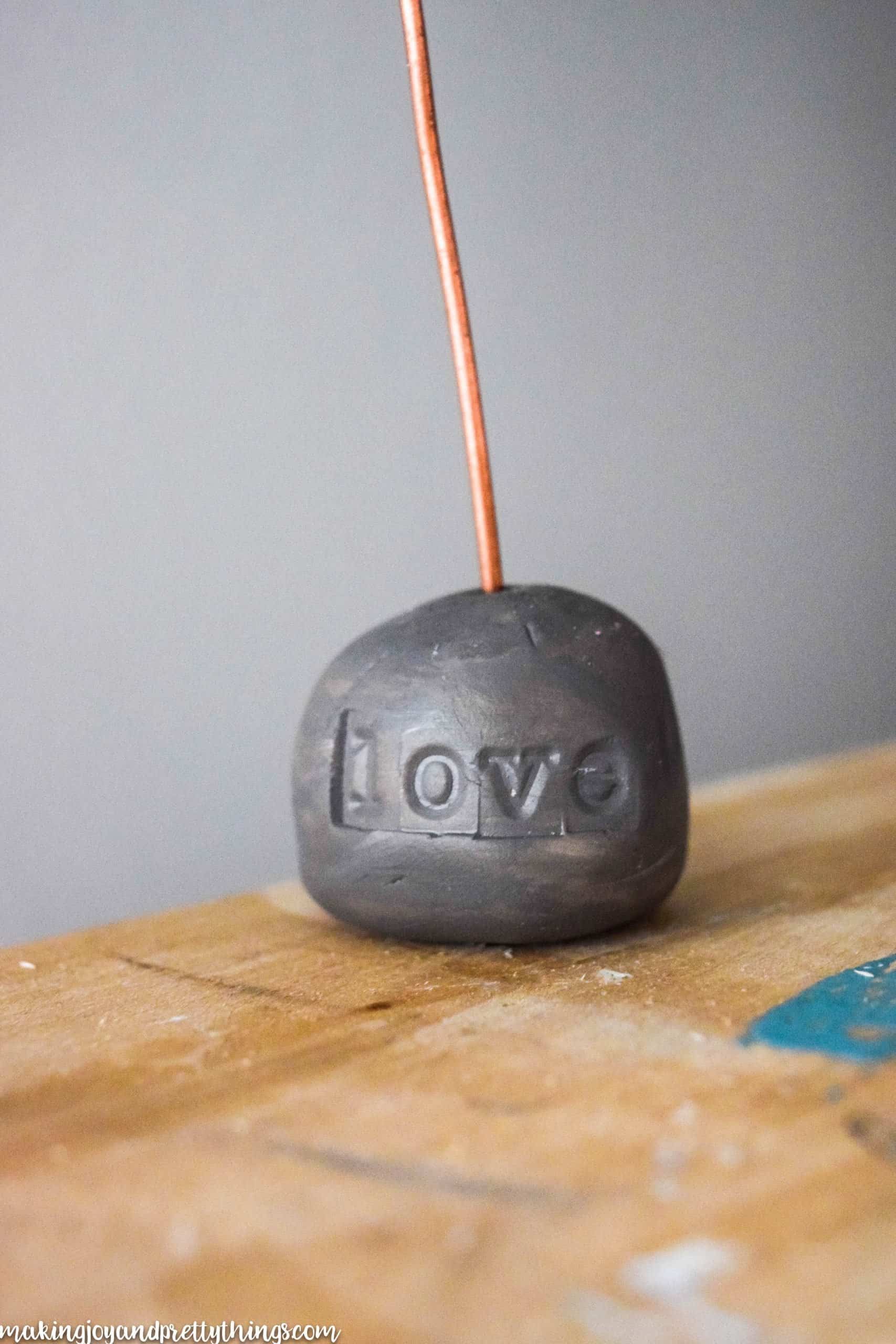 The word love on baked clay that has been painting grey with a copper wire coming out the top to hold pictures