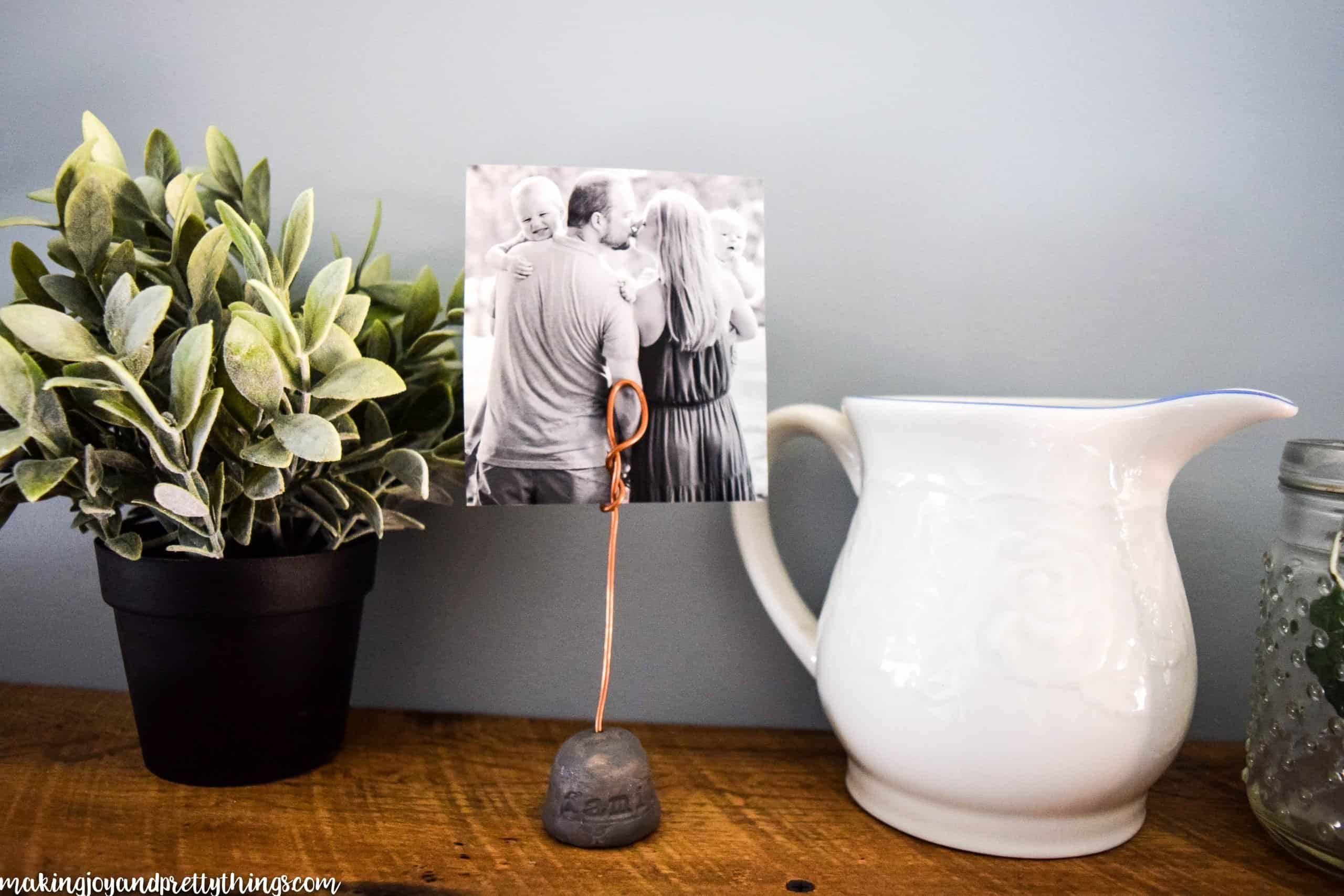 This DIY wire photo holder pairs well with other farmhouse decor such as plants and a white pitcher on rustic shelves