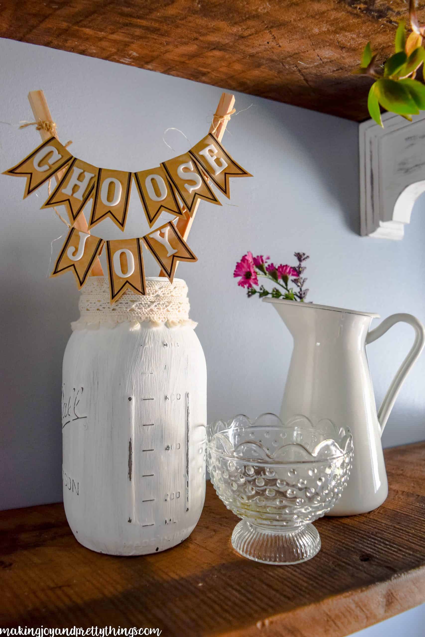 White pitcher with red flowers on rustic farmhouse shelves and other decor hung on a wall
