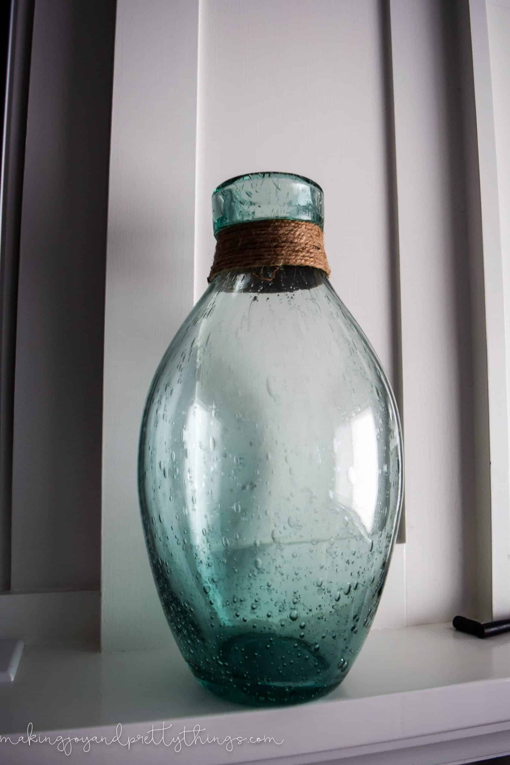 A blue seaglass bottle vase with jute string wrapped around the top. The glass vase has an ombre color effect from top to bottom, with air bubbles in the blown glass.
