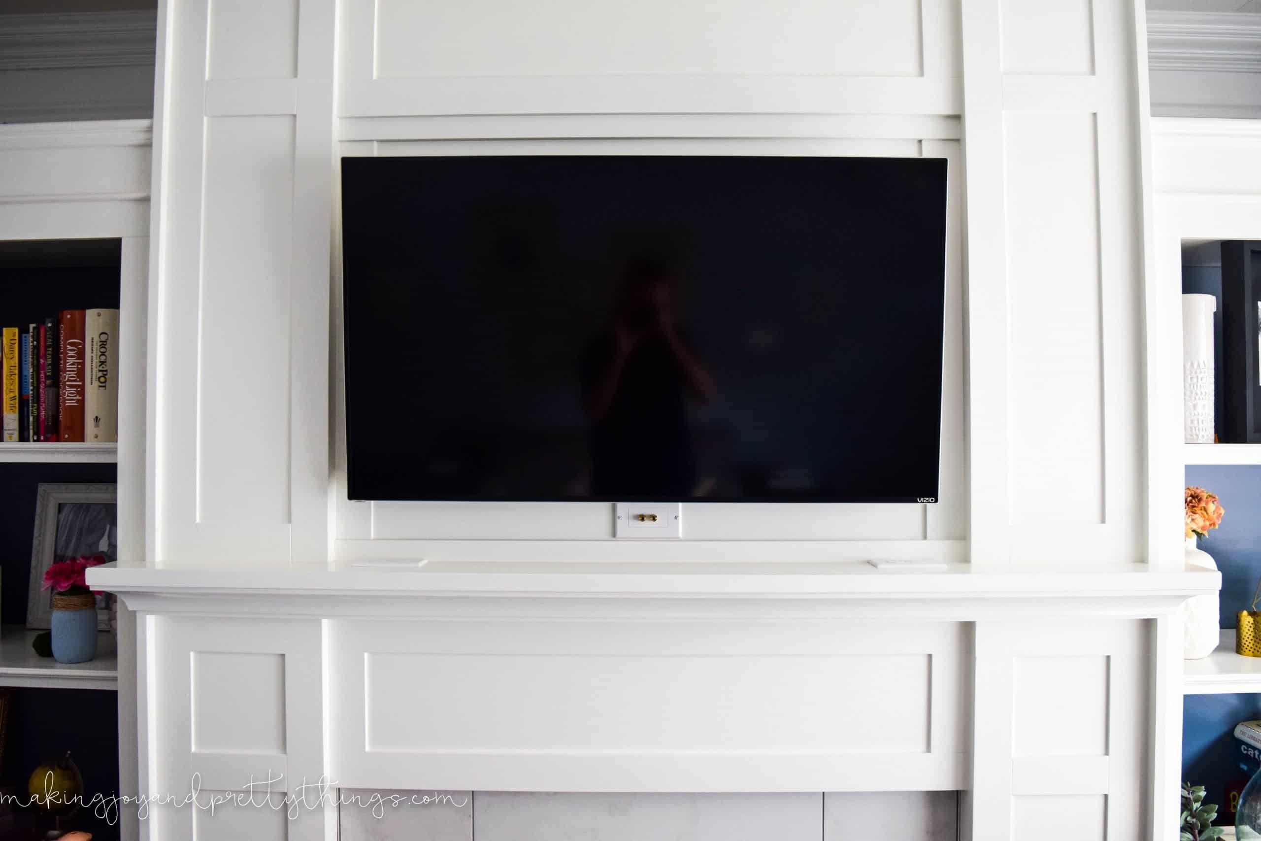 A plain white mantle with a large flat screen TV hanging in the center.