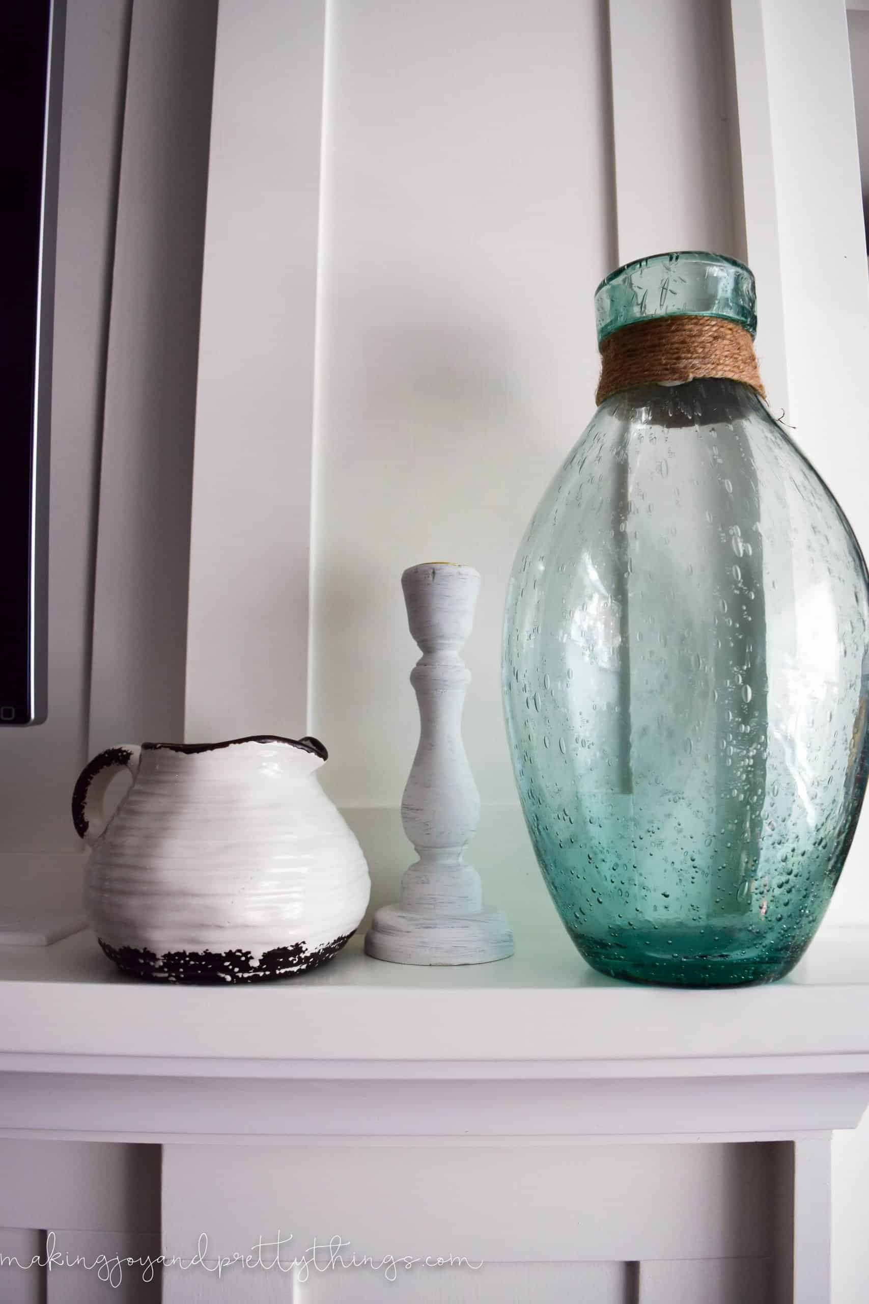 Some summer mantle decor pieces: a blue ombre seaglass vase wrapped with jute string, a rustic white candle holder, and black and white ceramic jug.