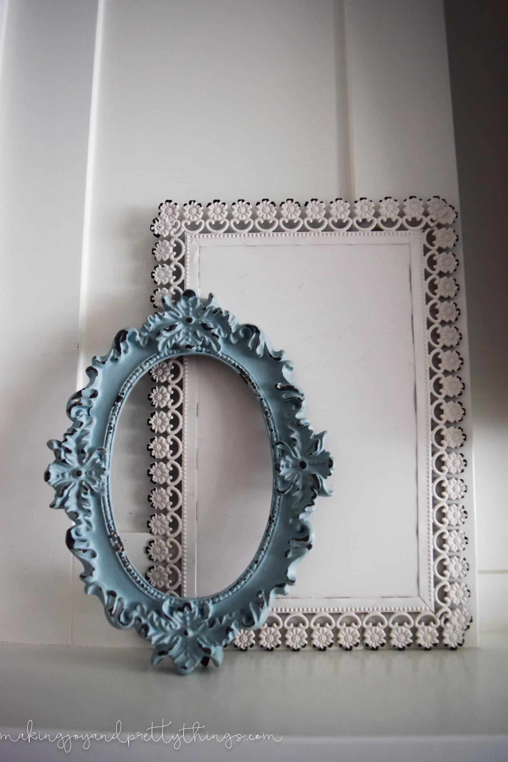 Two empty, mismatched farmhouse style frame. The front frame is a small teal blue oval frame; the background frame is white with a floral pattern around the edges.
