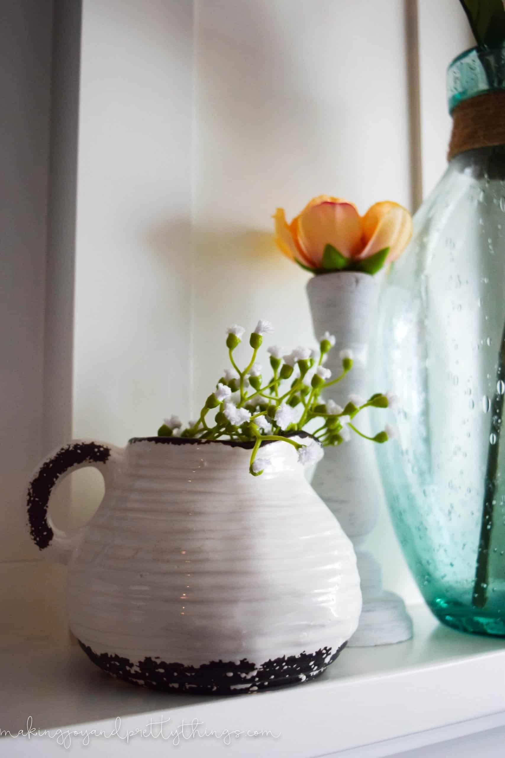 A close up look at one of the ceramic pottery vases, painted white and black, and filled with faux sprigs of greenery.