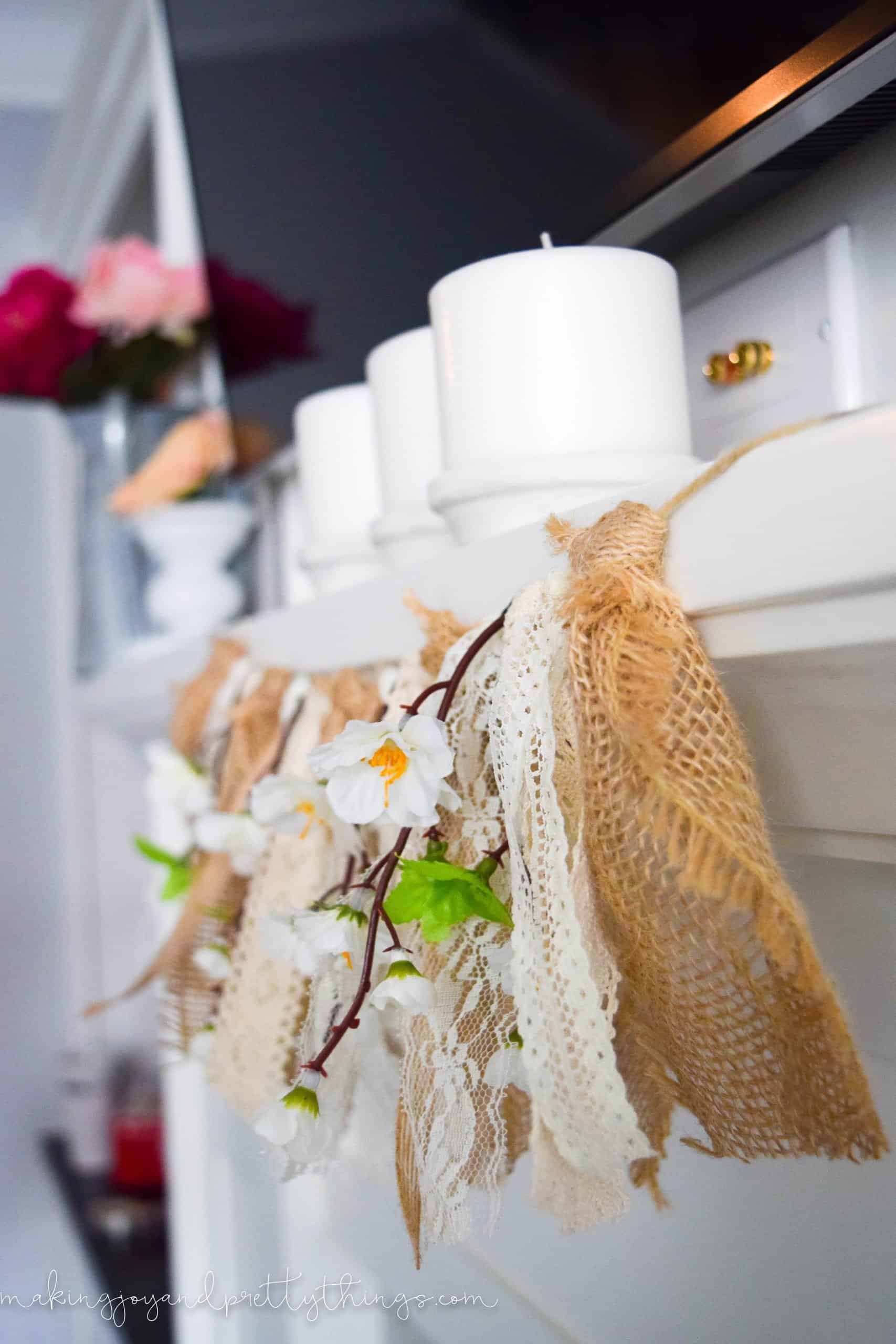 A close up look at the peach blossom garland that hangs across the mantle. Stems of faux peach blossoms hang between  pieces of burlap and lace fabric.