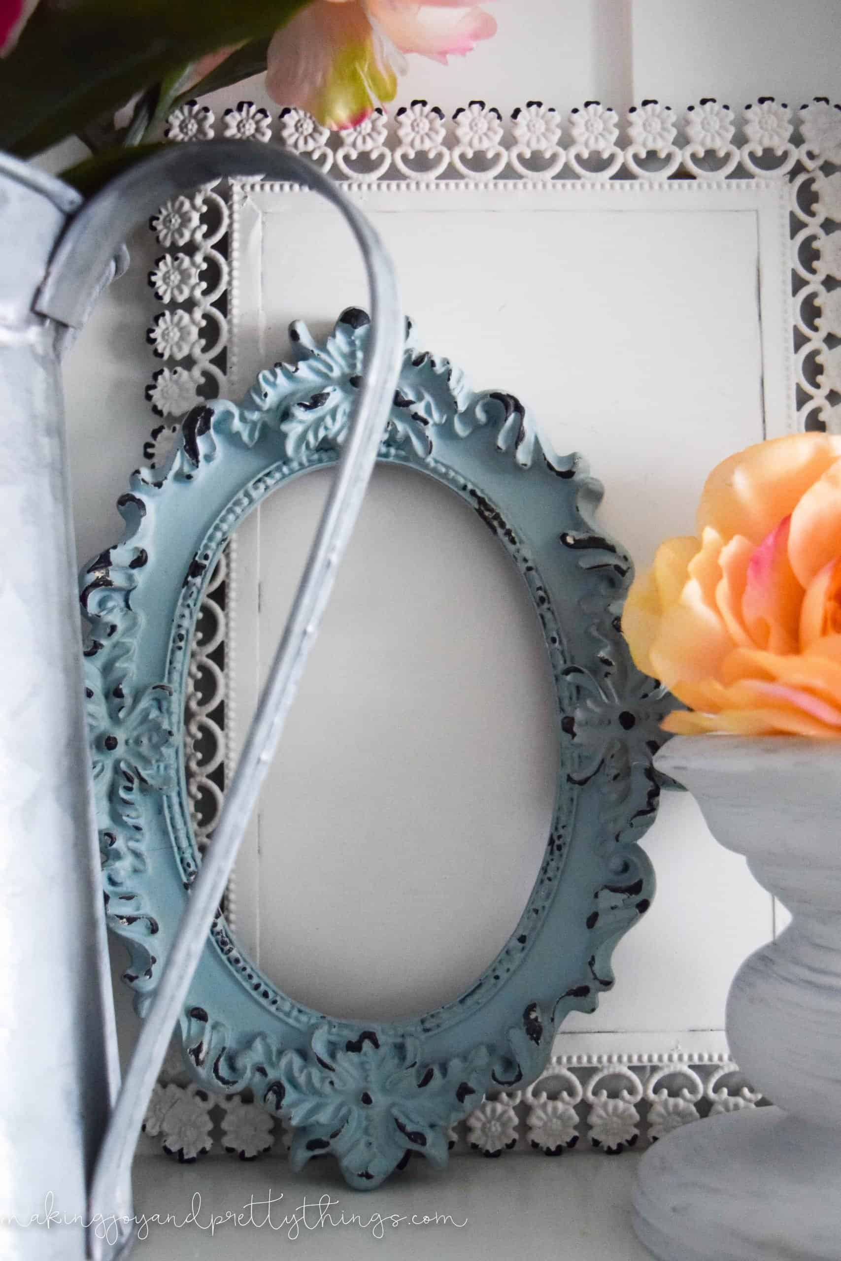 A close up look at one of the empty picture frames, painted a distressed tiffany blue color, with ornate carving around the frame.