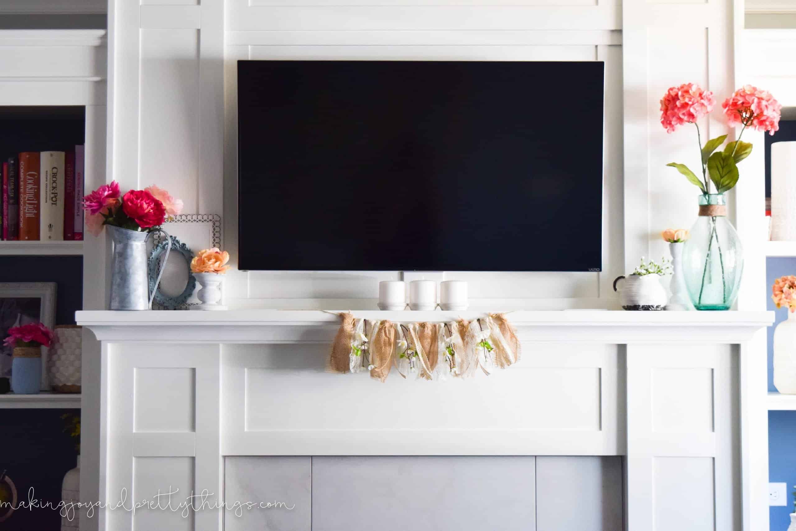 Our completed summer mantle decor - vases of faux flowers, pottery, candle holders, and a peach blossom garland surround our wall-mounted TV.