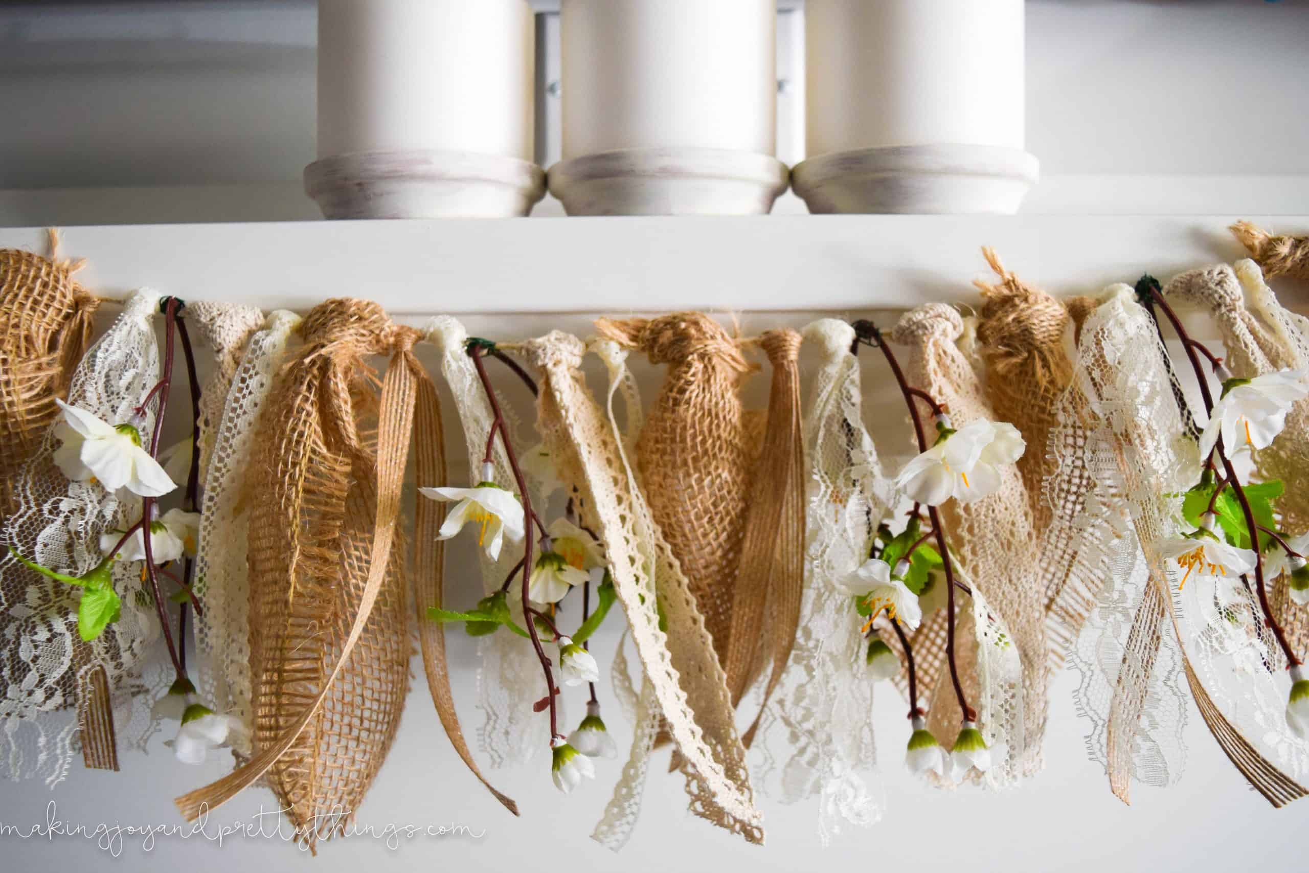 A close up look at the peach blossom garland with faux florals, lace, and burlap fabric hangs across a white mantle.