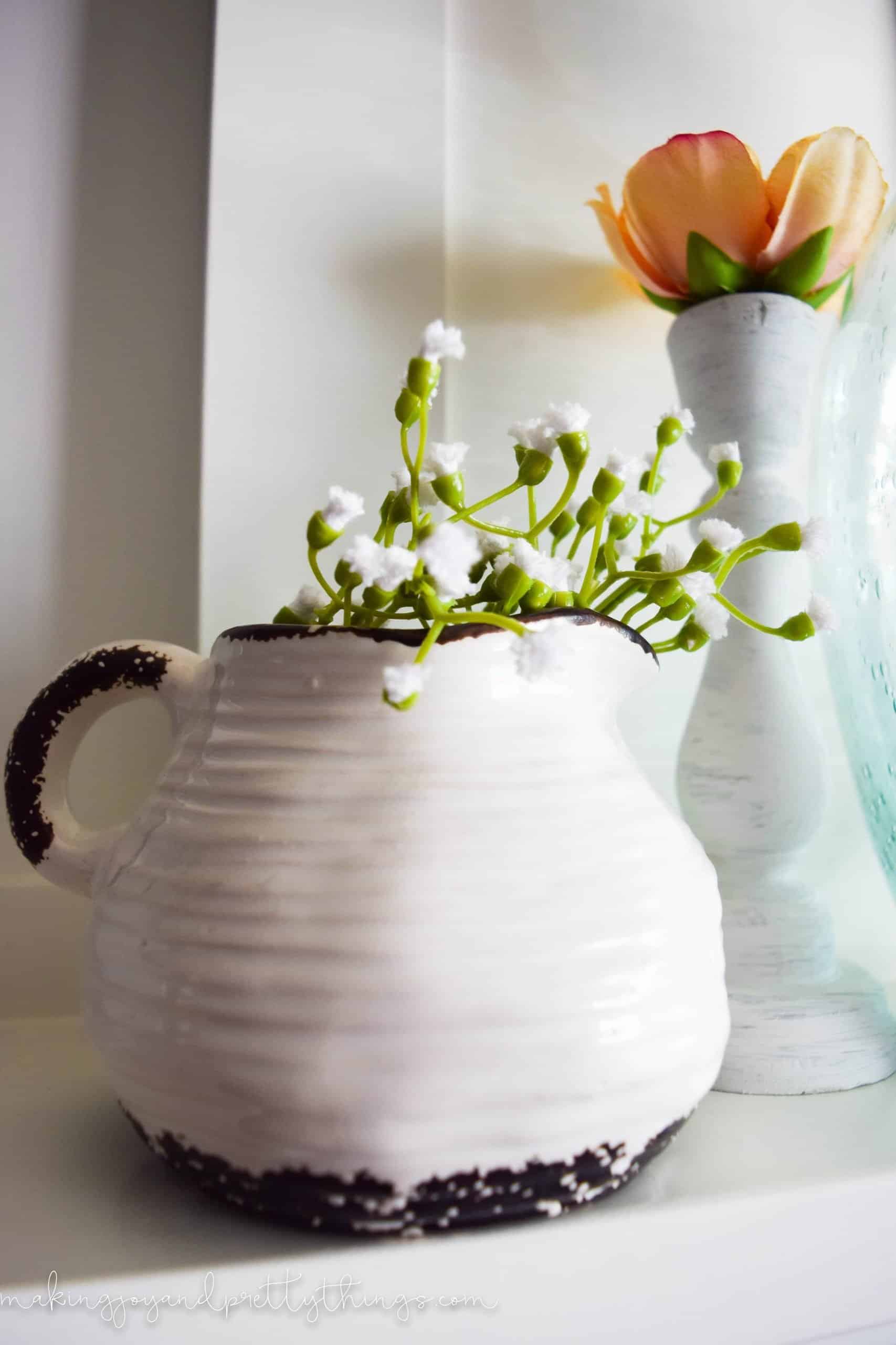 A close up look at a ceramic jar painted black and white, filled with sprigs of faux greenery with tiny white flower buds on the end.