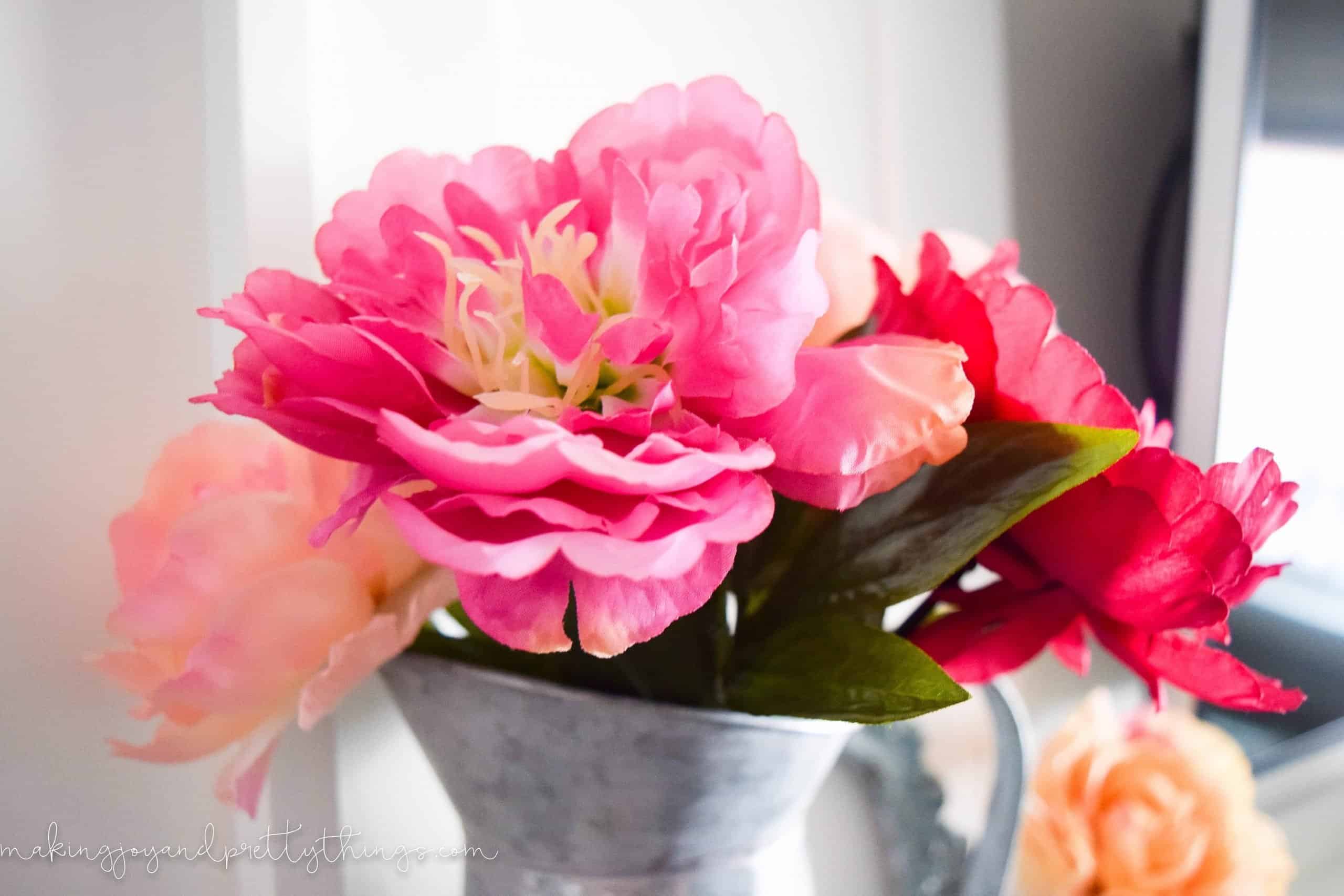 Stems of faux florals in varying shades of pink in a galvanized metal vase.