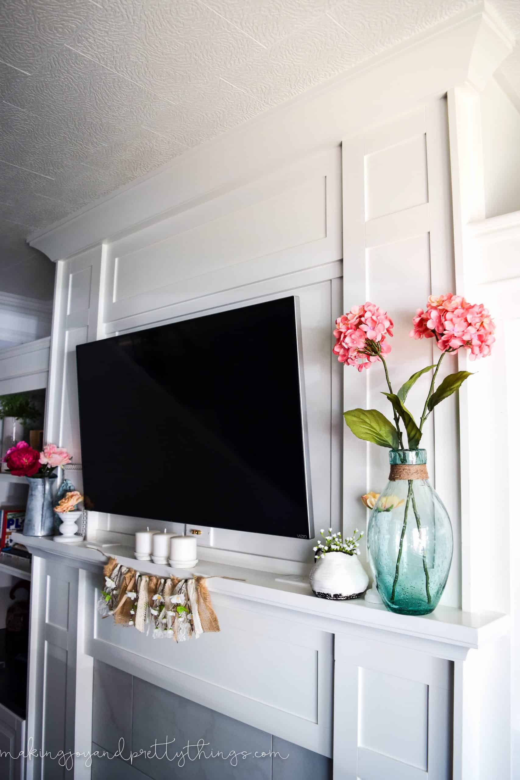 Another angle of our summer mantle decor, decorated with vases of faux flowers, a farmhouse peach blossom garland, pottery, and candle holders.