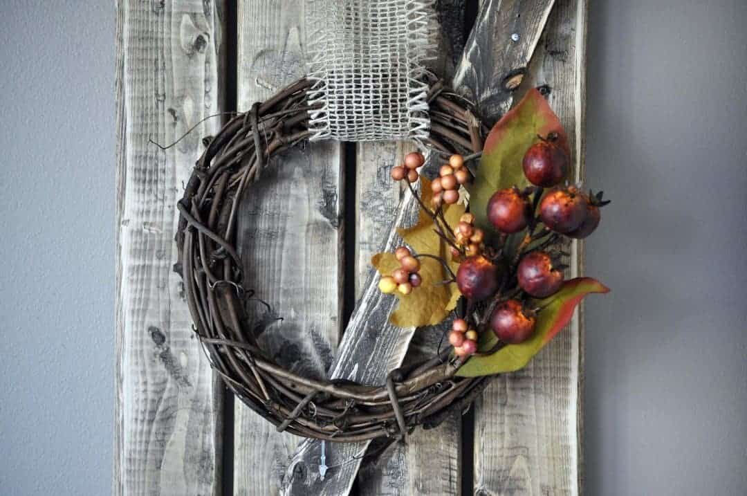 DIY fall wreath with floral notes faux pomegranate and berry plants tucked into the wreath with a burlap hanging