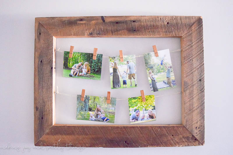 A DIY rustic picture frame hangs on a white wall. Five family photos hang from twine with clothespins.