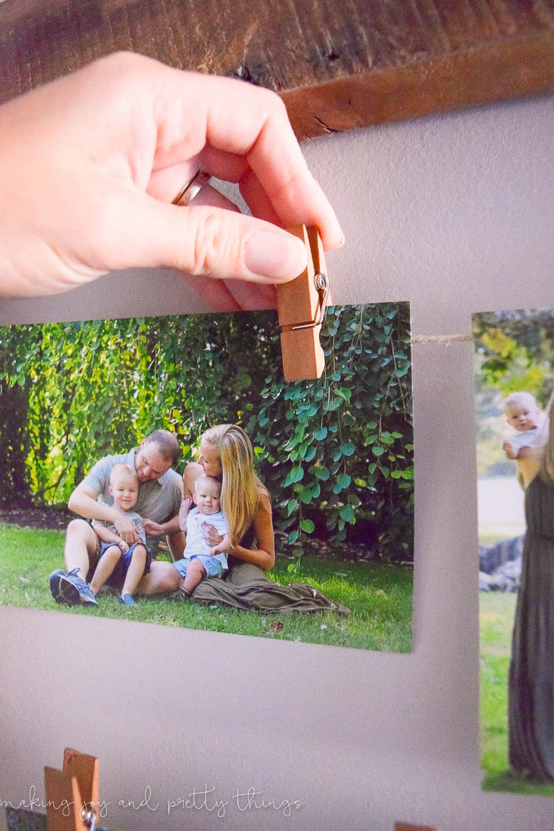 An image shows a hand using a small clothespin to hang a photo on a string of twine. The photo is of a family sitting outside in a yard.