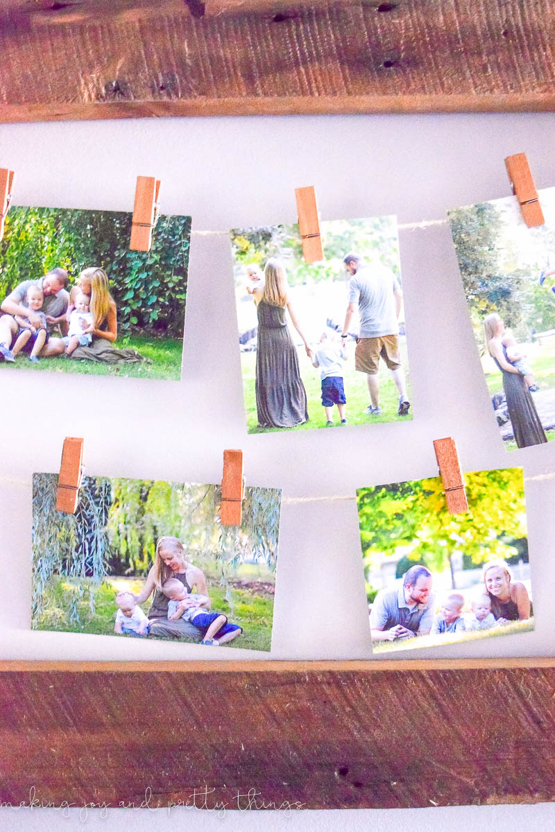 A closeup look at the family photos hanging in the rustic picture frame. Five photos are clipped to strings of twine with picture wire. The photos feature a family - mother, father, and two young children, playing happily outside and posing for the camera.