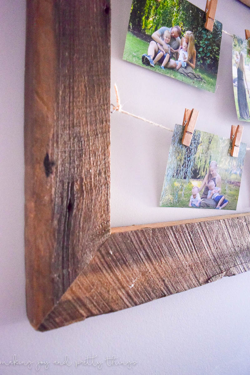 A close up look at the rustic wood used to make a picture frame. There are grooves in the wood and darker stained spots. Strings of twine in the picture frame hold family photos.
