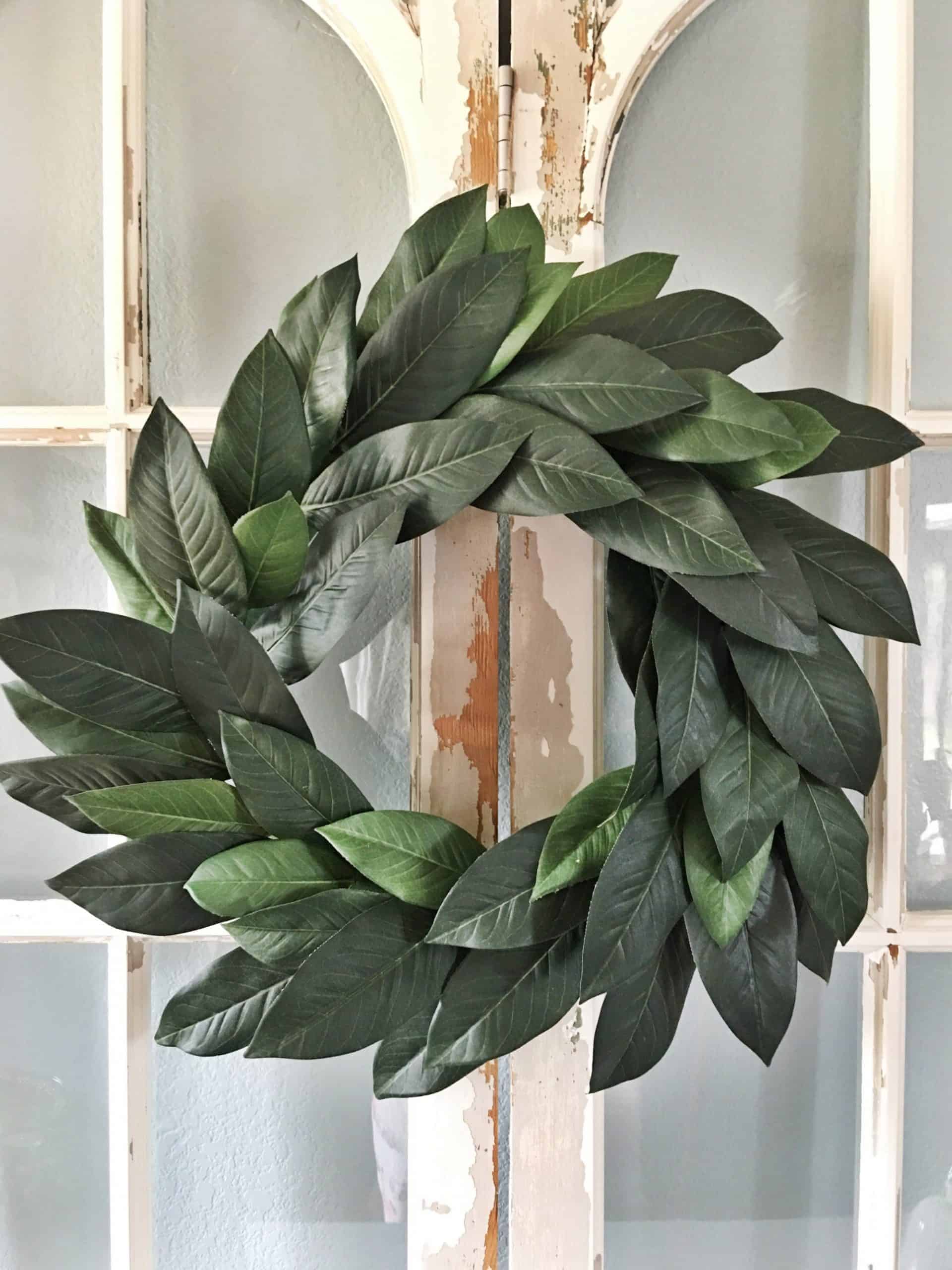 Faux wreath made with magnolia leaves hanging on chipped paint windows with farmhouse style