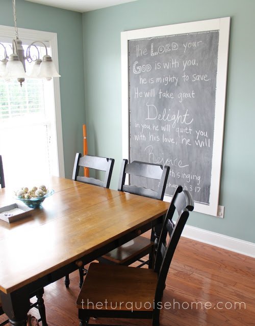 Giant chalkboard with a white frame hanging on the wall in a dining room with a bible verse written on it