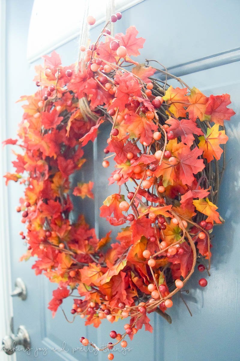 A vibrant red, orange, and yellow DIY fall leaf wreath hangs from twine on a teal front door.