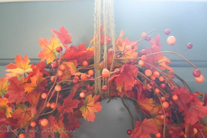This DIY Fall leaf wreath hangs on a door with strands of twine looped around the top of the wreath.