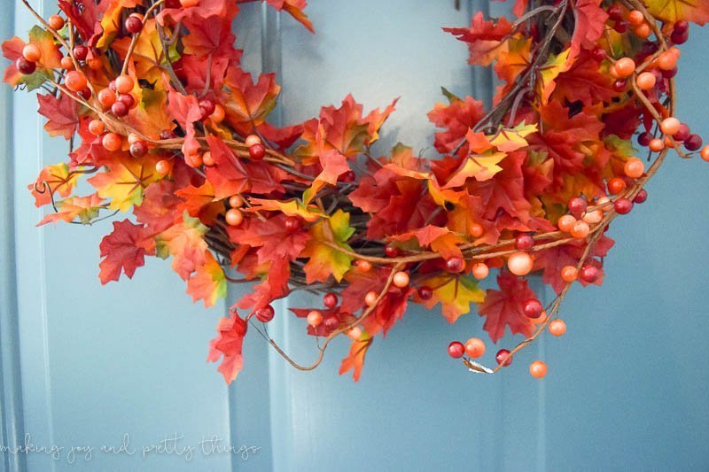 A closer look at the details of this DIY leaf wreath - vibrant faux fall-colored leaves with strands of faux berries sprinkled in.