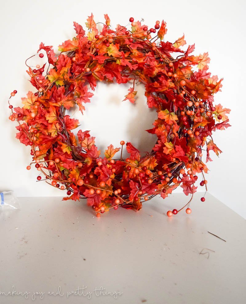 A completed DIY fall leaf wreath with vibrant orange and red leaves and faux berries wrapped around a grapevine wreath.