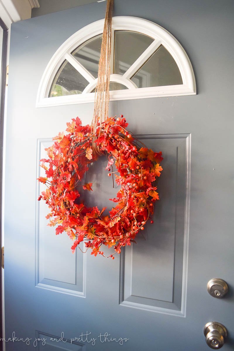 A completed DIY fall-inspired faux leaf wreath hangs from a length of looped twine against a grey-colored front door.