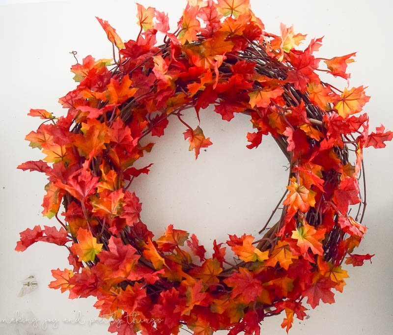 A vibrant Fall leaf wreath made from strands of orange and red Fall leaves wrapped around a grapevine wreath frame.