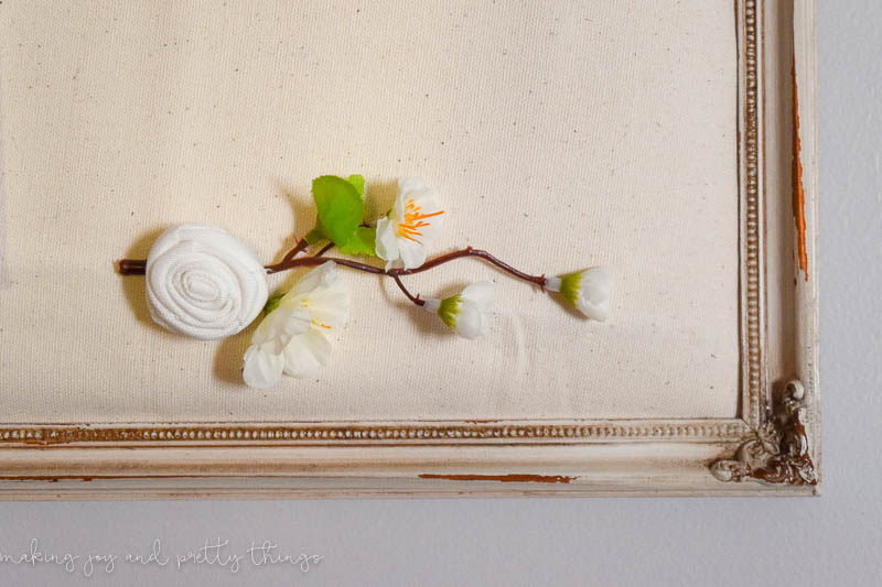 Cute faux floral branch with leaves and flowers pinned up with DIY push pins into a muslin covered cork board