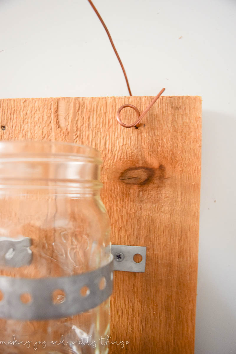 Threading copper wire through the wood plank in order to provide a rustic farmhouse way to hang the mason jar