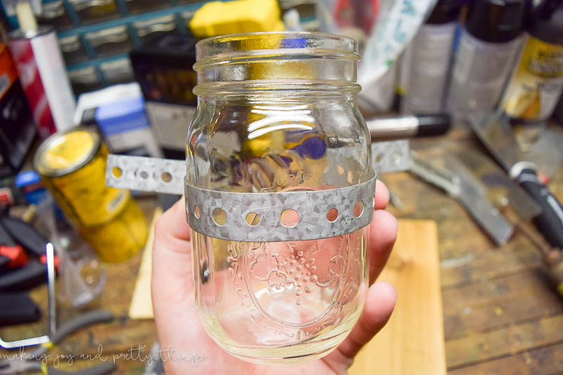 Wrapping pipe strap around the mason jar to create a way to hang it on the cedar plank wood 