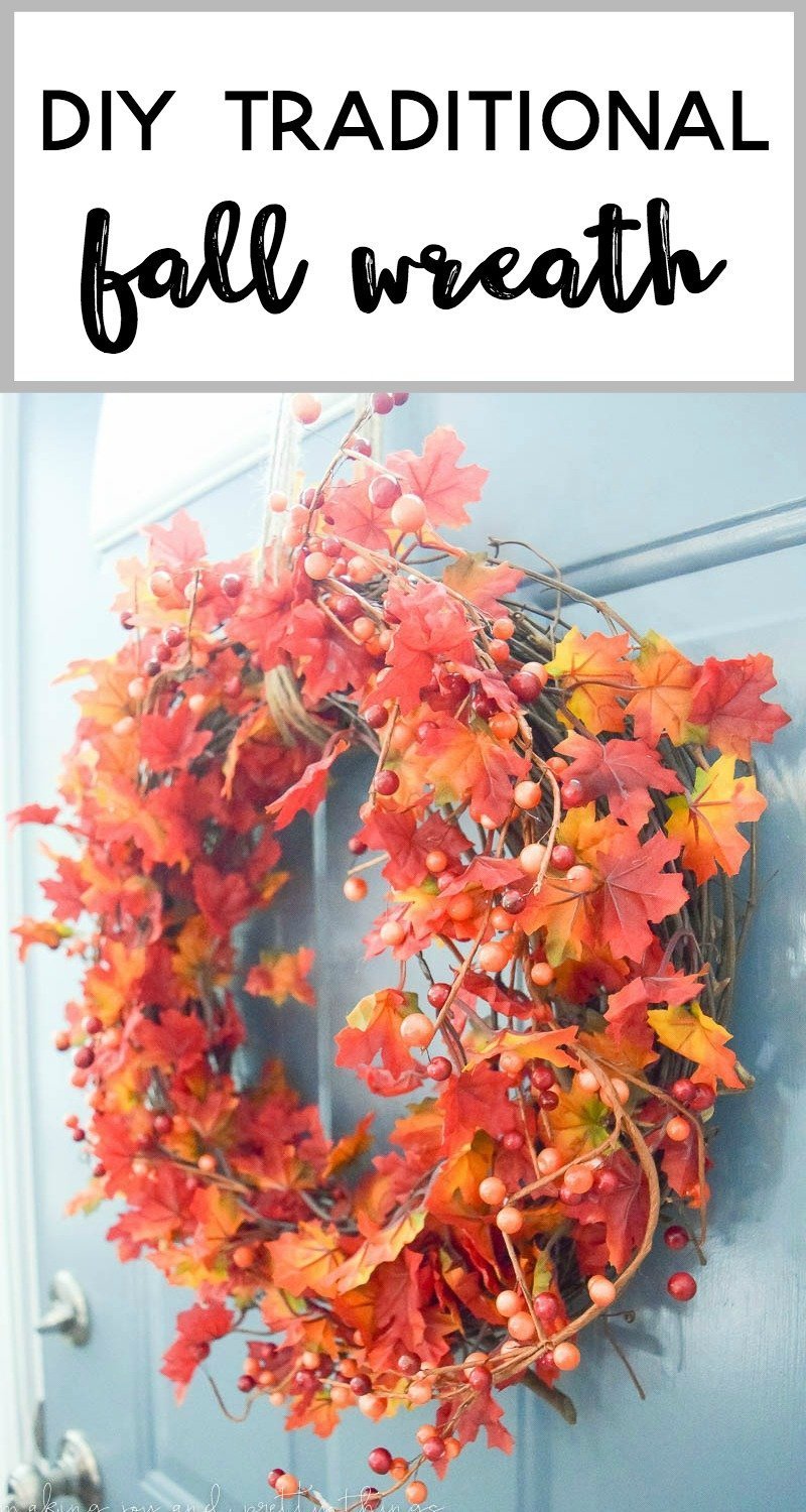 A bright and colorful fall leave wreath hangs on a teal front door. The faux leaves are bright orange and yellow, with orange and red berries and twigs, all in a round grapevine wreath.