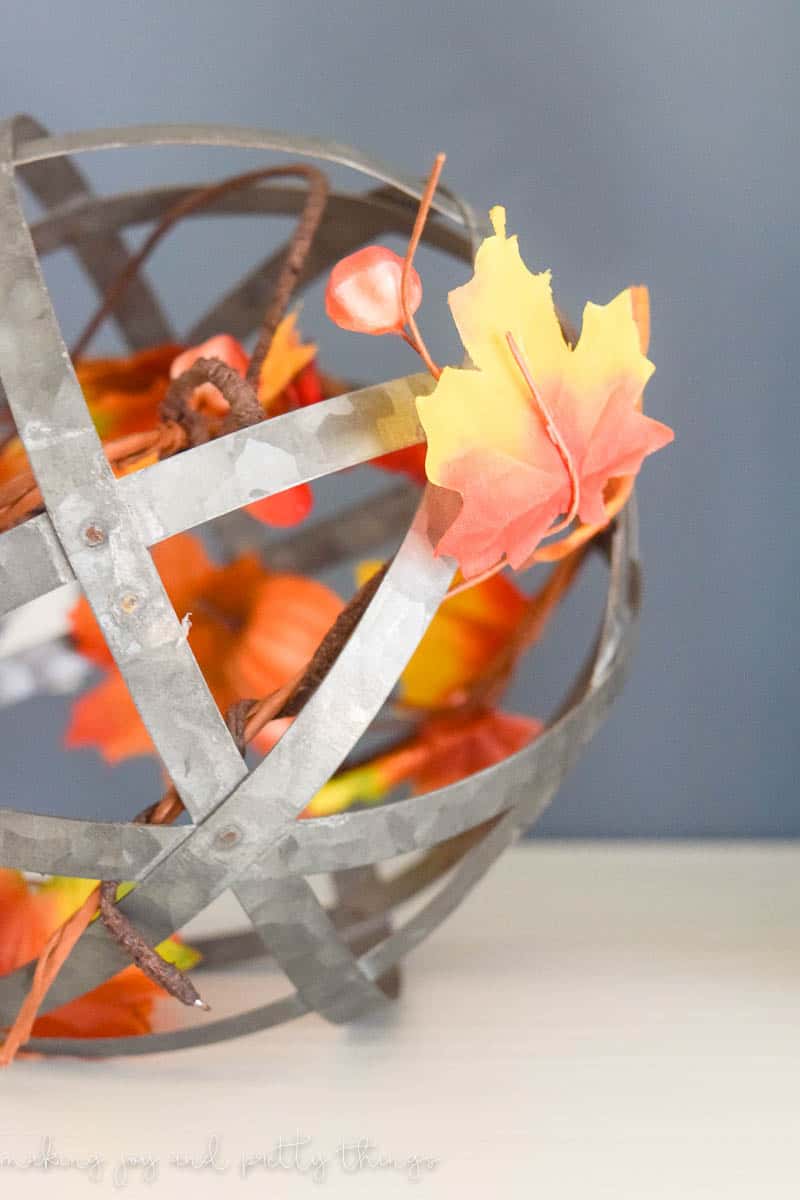 A metal globe statue filled with orange and yellow faux leaves.