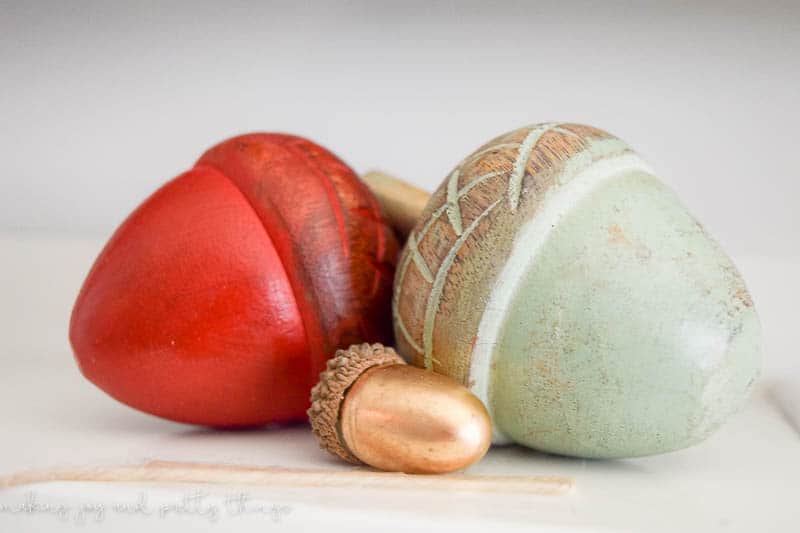 A close up look at a set of three wooden acorns - one is orange, a mint green, and a smaller gold acorn - sitting on the living room mantle.